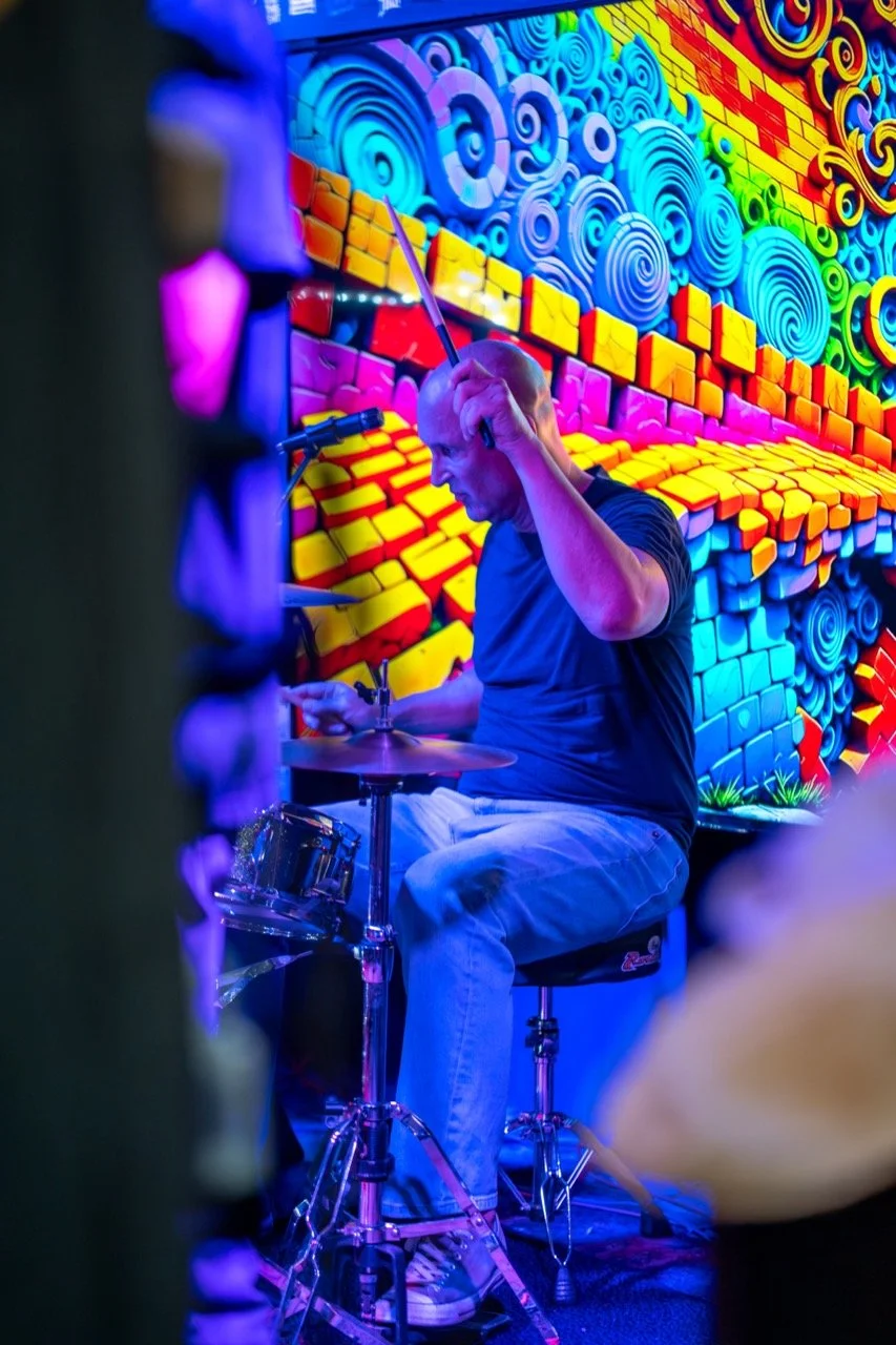 A person playing drums in a vibrant, colorful room with psychedelic wall art.