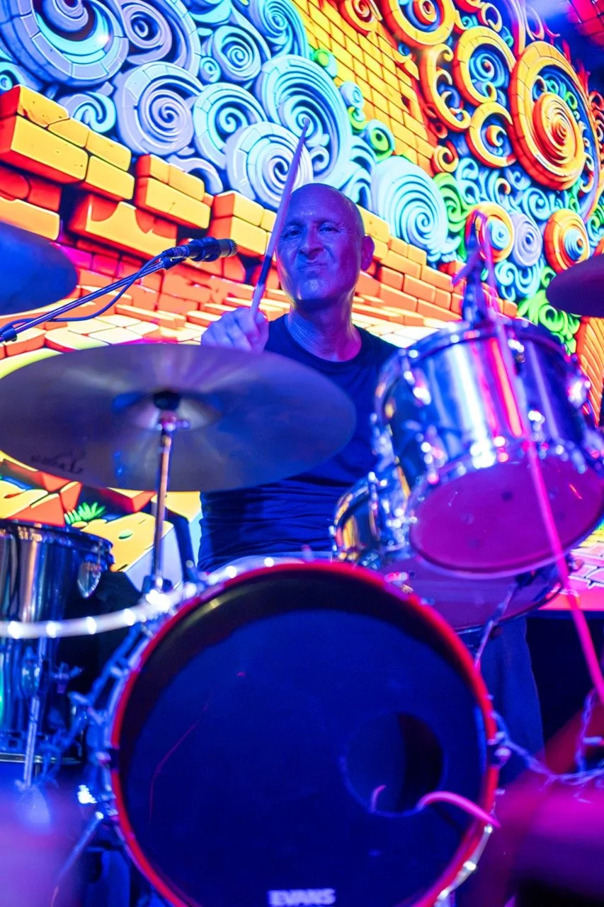 A man playing drums on stage with a colorful, swirling background