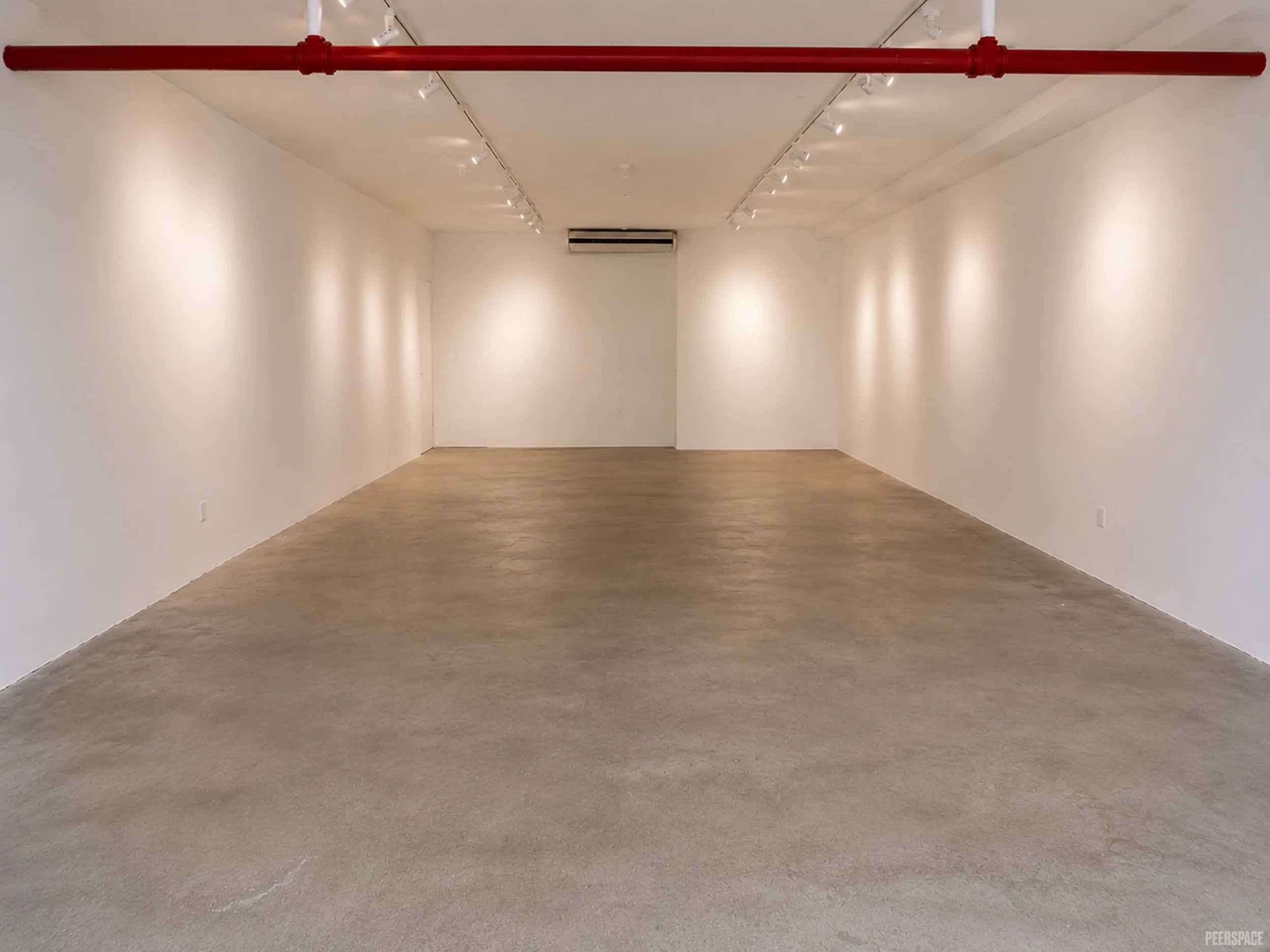 Empty gallery room with white walls, wooden floor, red pipe on ceiling, and a central air conditioning unit mounted on the back wall.
