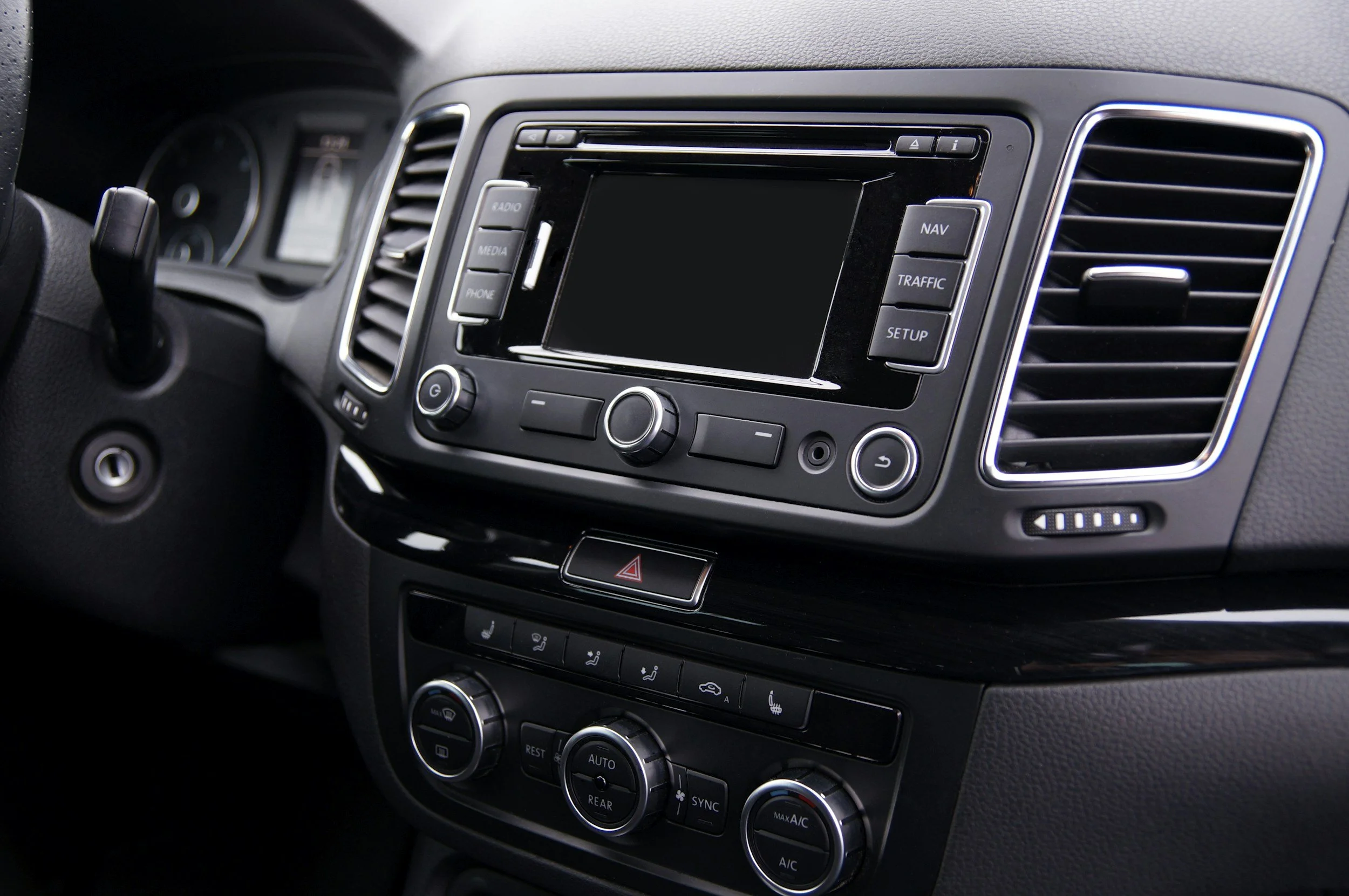 Dit is het interieur van een auto, met een centraal dashboard dat een touchscreen display en knoppen bevat voor media, navigatie, en klimaatregeling.
