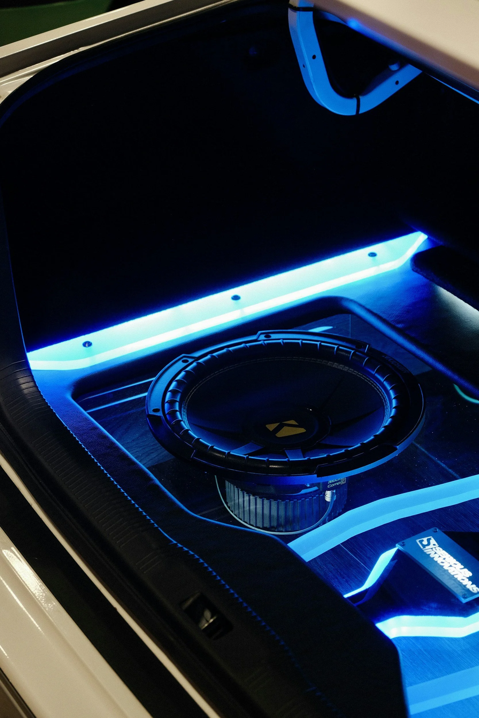Close-up van een audio-installatie met een subwoofer en blauwe LED-verlichting onder een glasplaat.