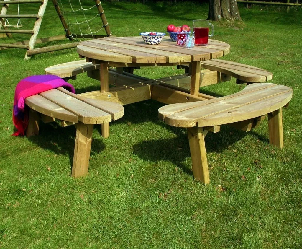 Wooden picnic table with attached benches on grass, decorated with bowls of apples, jars, and a pitcher, outdoors in a park or backyard.