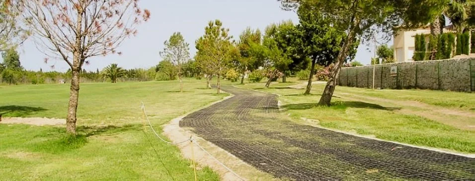 A winding pathway under construction in a grassy park with trees and a stone fence in the background.