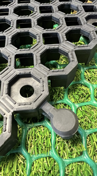 A close-up view of a green and black plastic object, likely part of a gardening or sports equipment, on a small patch of grass.