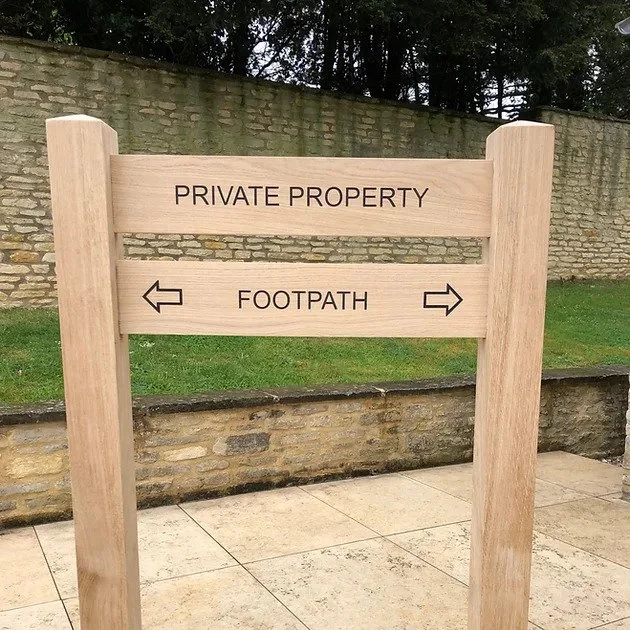 A wooden sign with the words 'Private Property' at the top and arrows pointing left and right labeled 'Footpath'