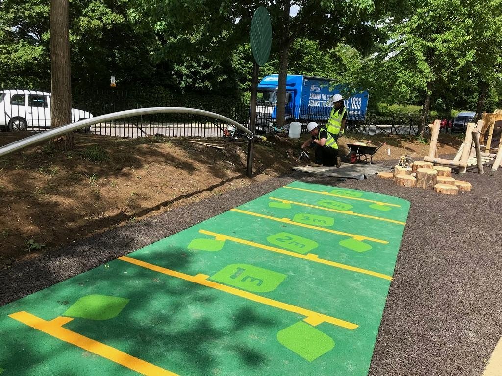 Children's outdoor playground with a hopscotch game painted on the ground, and workers installing equipment nearby.