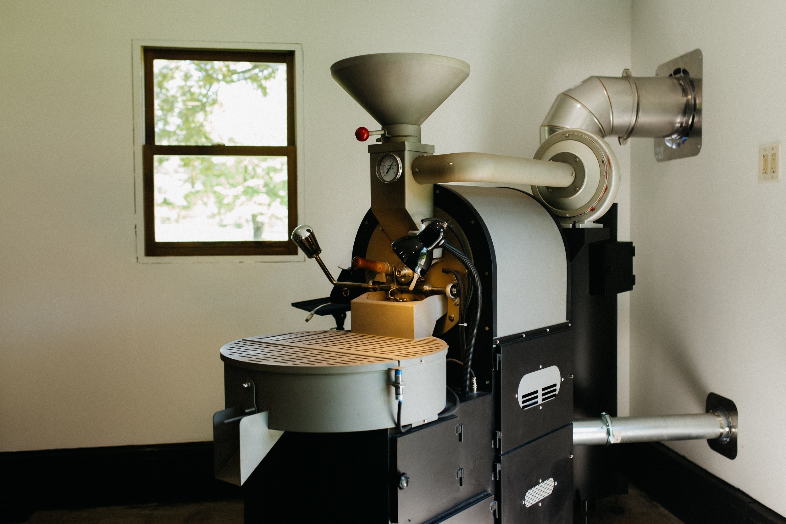 A machine used in coffee grinding inside a room with a window showing trees outside.