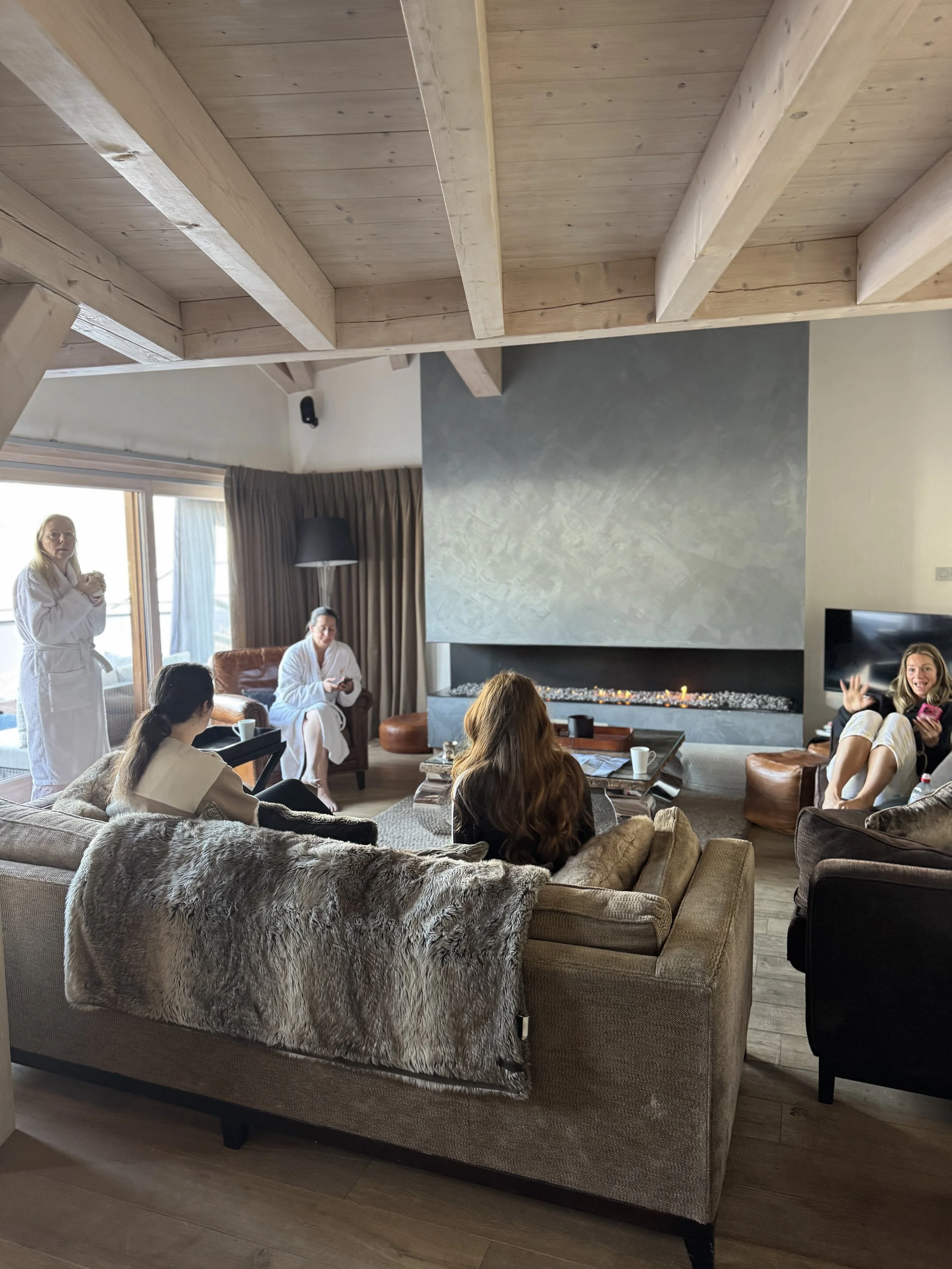 People in a living room wearing bathrobes, some sitting on a sofa, others standing near a fireplace and window, appearing to socialize.