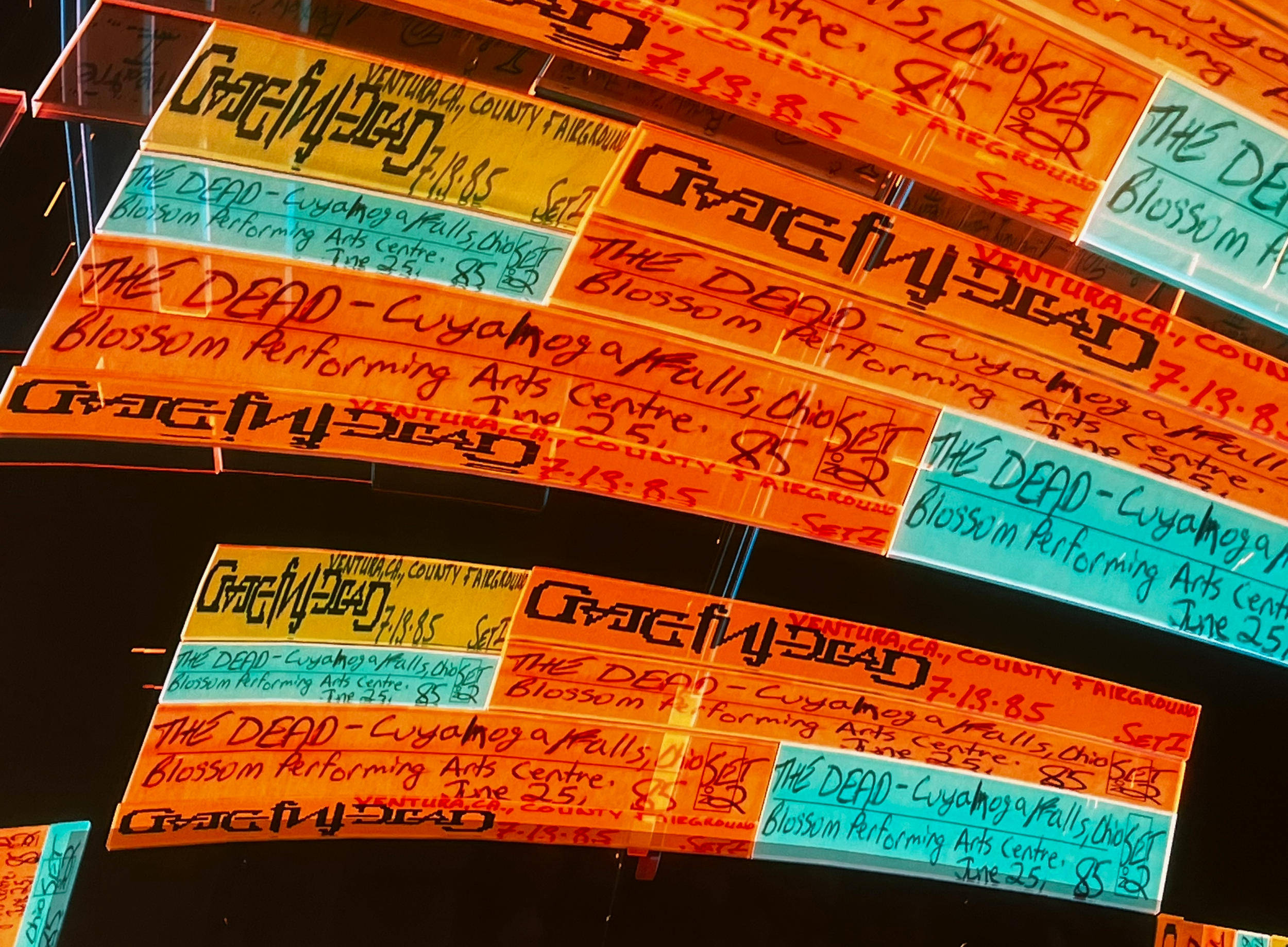 Multiple colorful neon signs hanging in a row, advertising 'The Dead' at Cuyahoga Falls Blossom Performing Arts Center on June 25, with ticket prices of $7.18 and $8.85.
