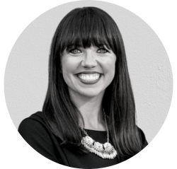 Portrait of a smiling woman with straight dark hair, wearing a black outfit and a statement necklace, in black and white.