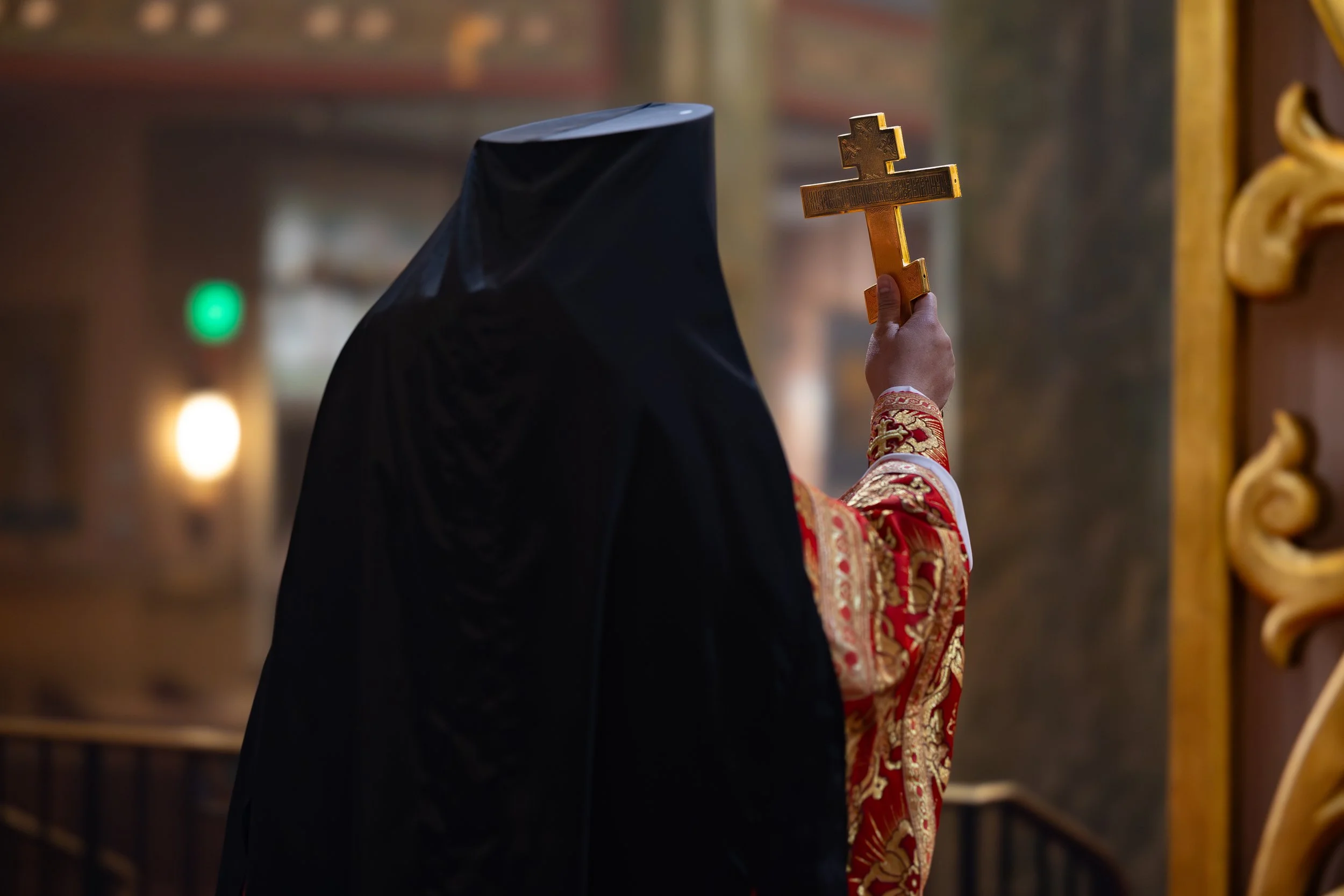 A person dressed in religious attire holding a gold cross in a church or cathedral.