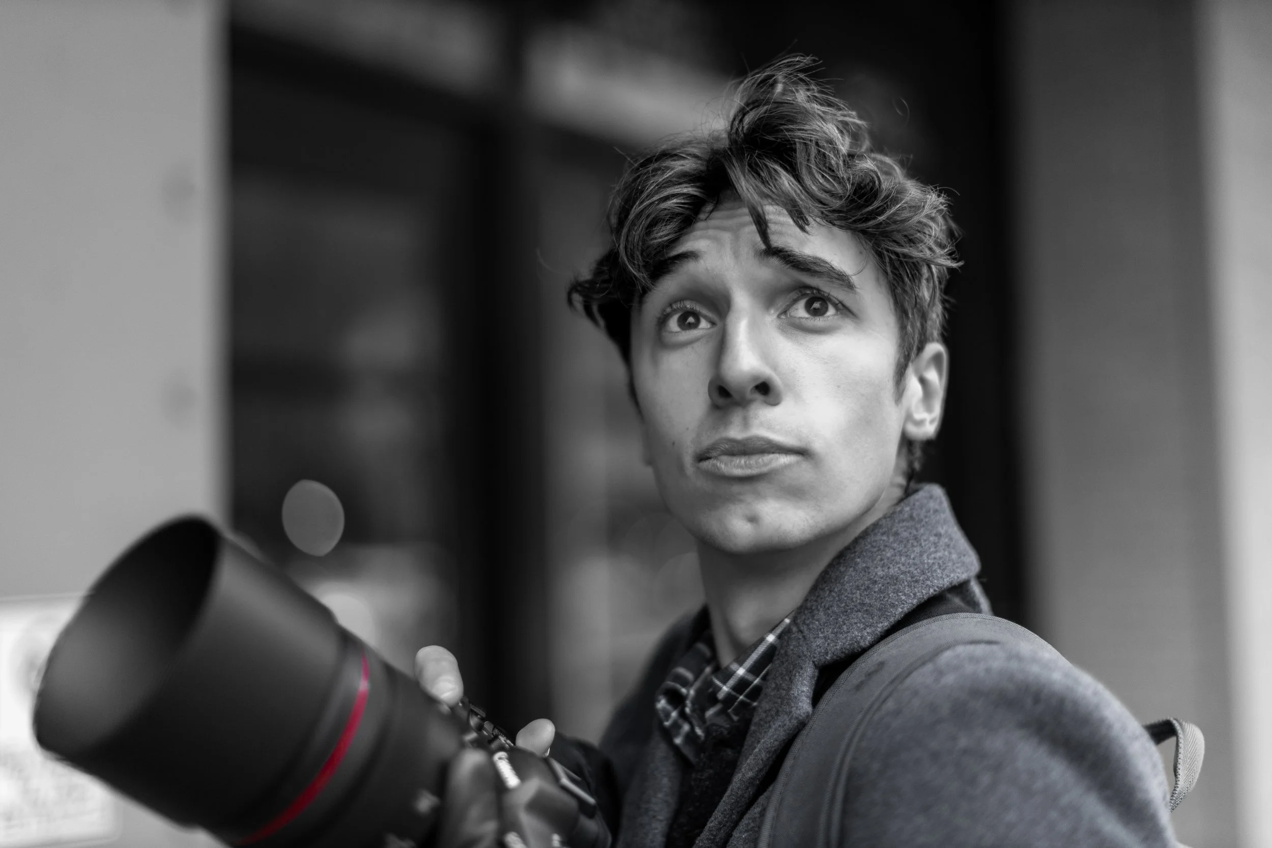 Black and white photo of a young man with wavy hair, looking upward while holding a camera.