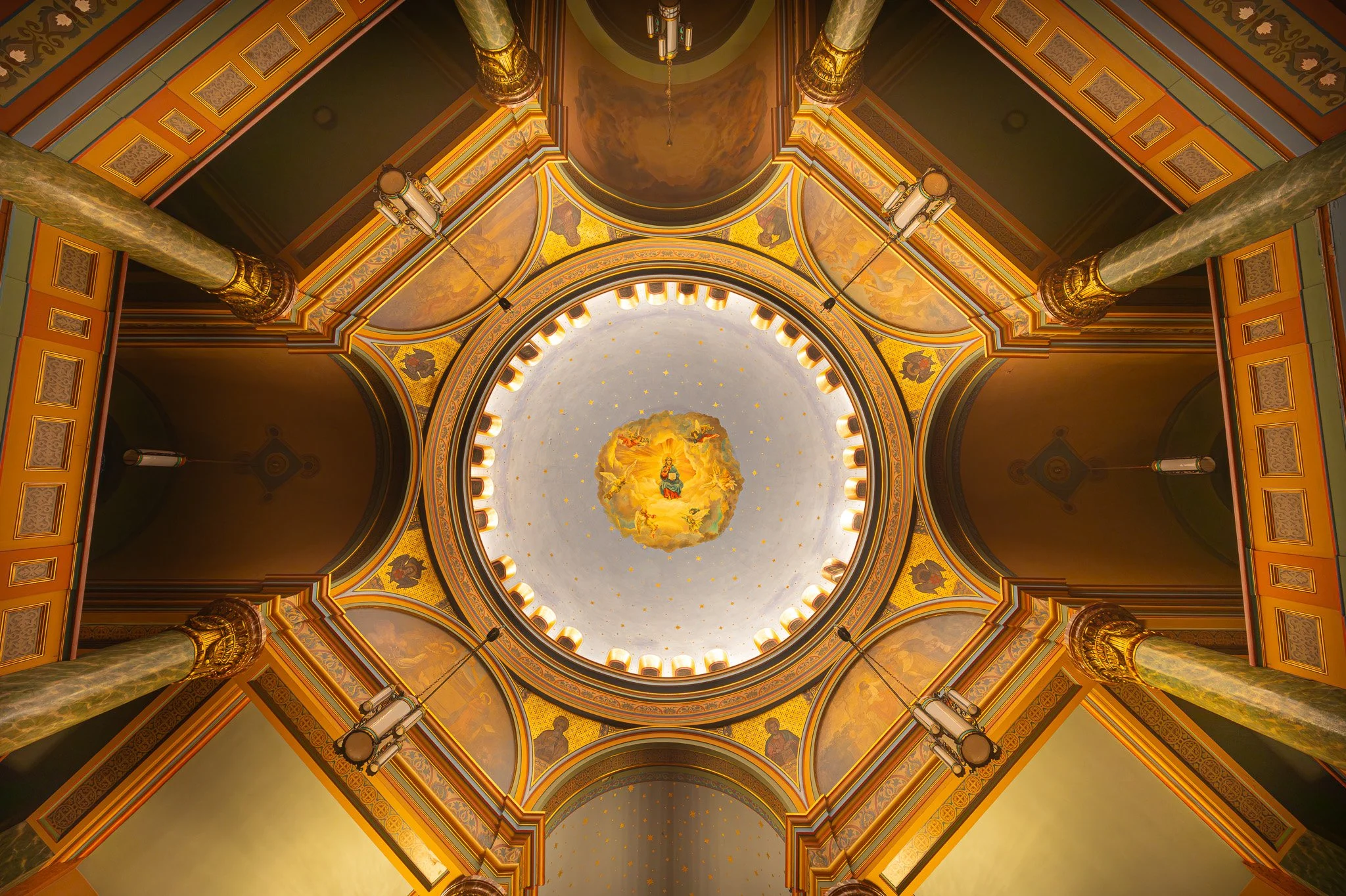 The interior ceiling of a church with ornate columns, detailed gold and green decor, and a central painting of angels and divine figures in the dome.