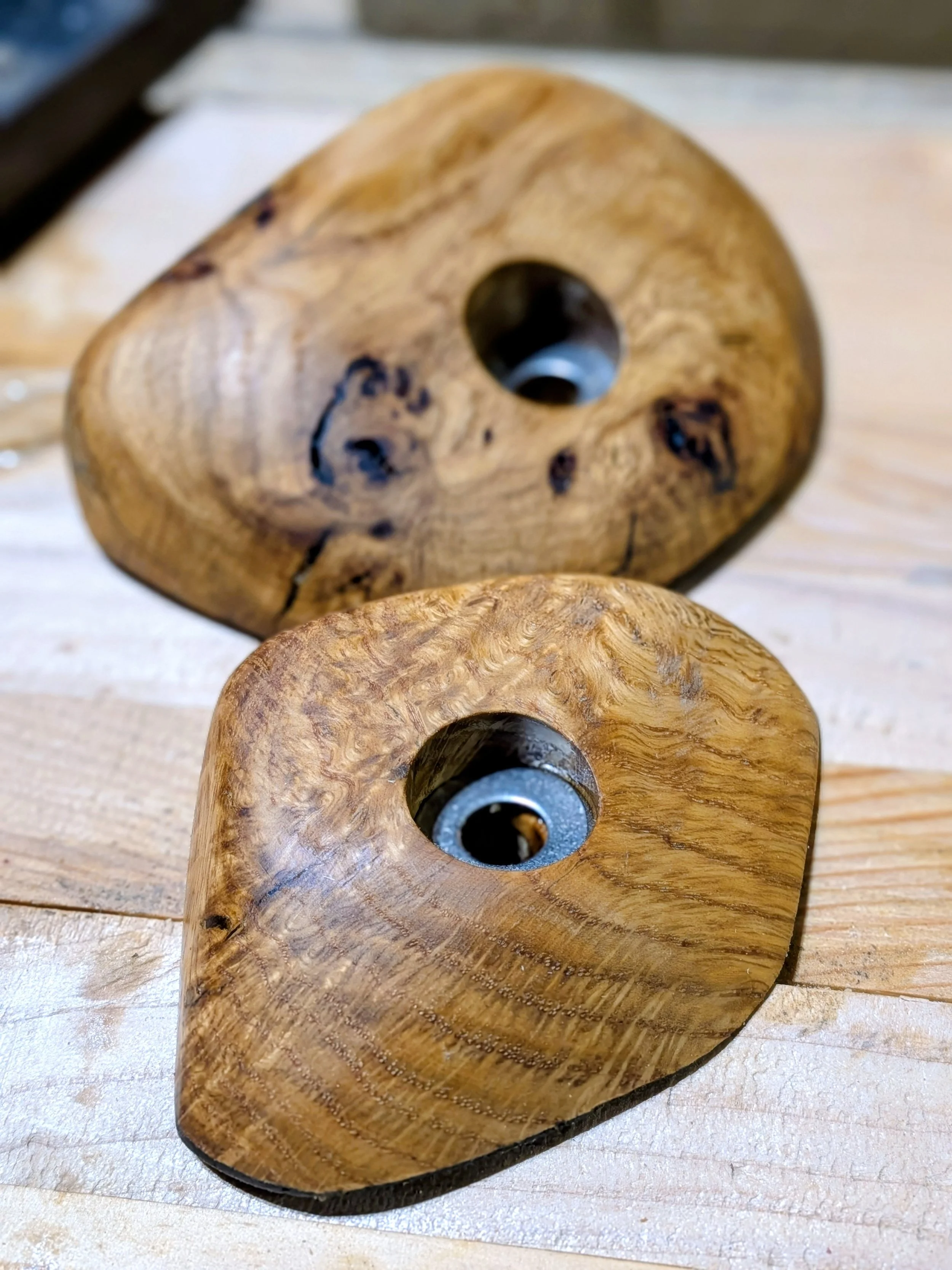 Close-up of two wooden objects with metal inserts on a light wooden surface.