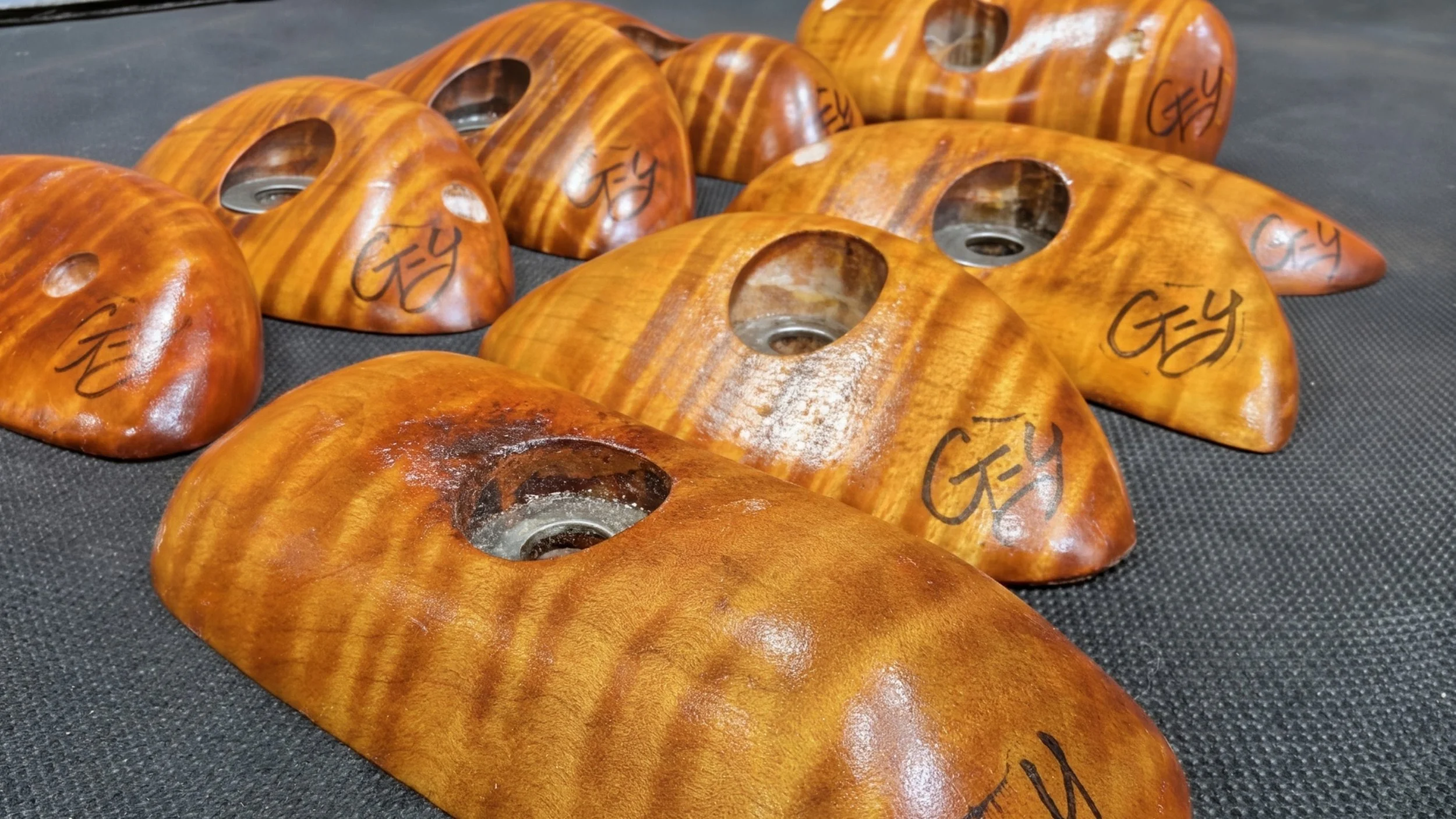 Multiple wooden hold shapes with the brand name 'Gey' written on each, arranged on a black surface, used for rock climbing training.