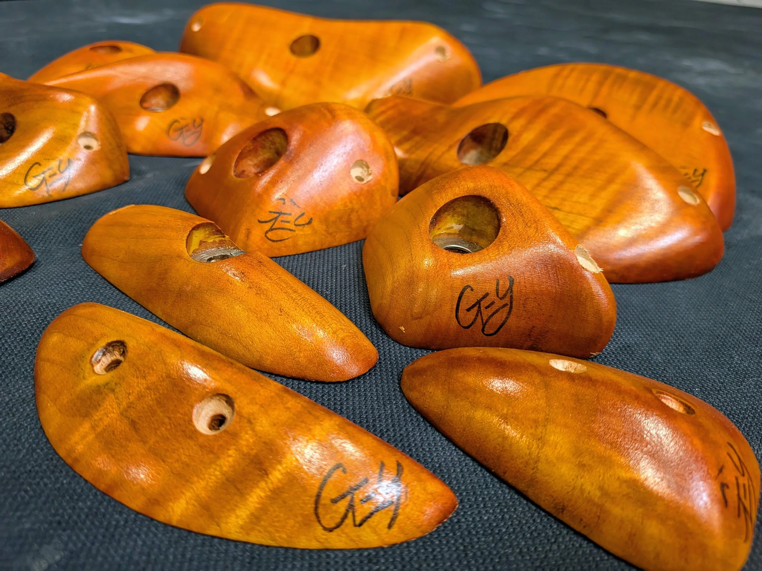 Multiple wooden bowling balls with holes, arranged on a dark surface, with handwriting on them.