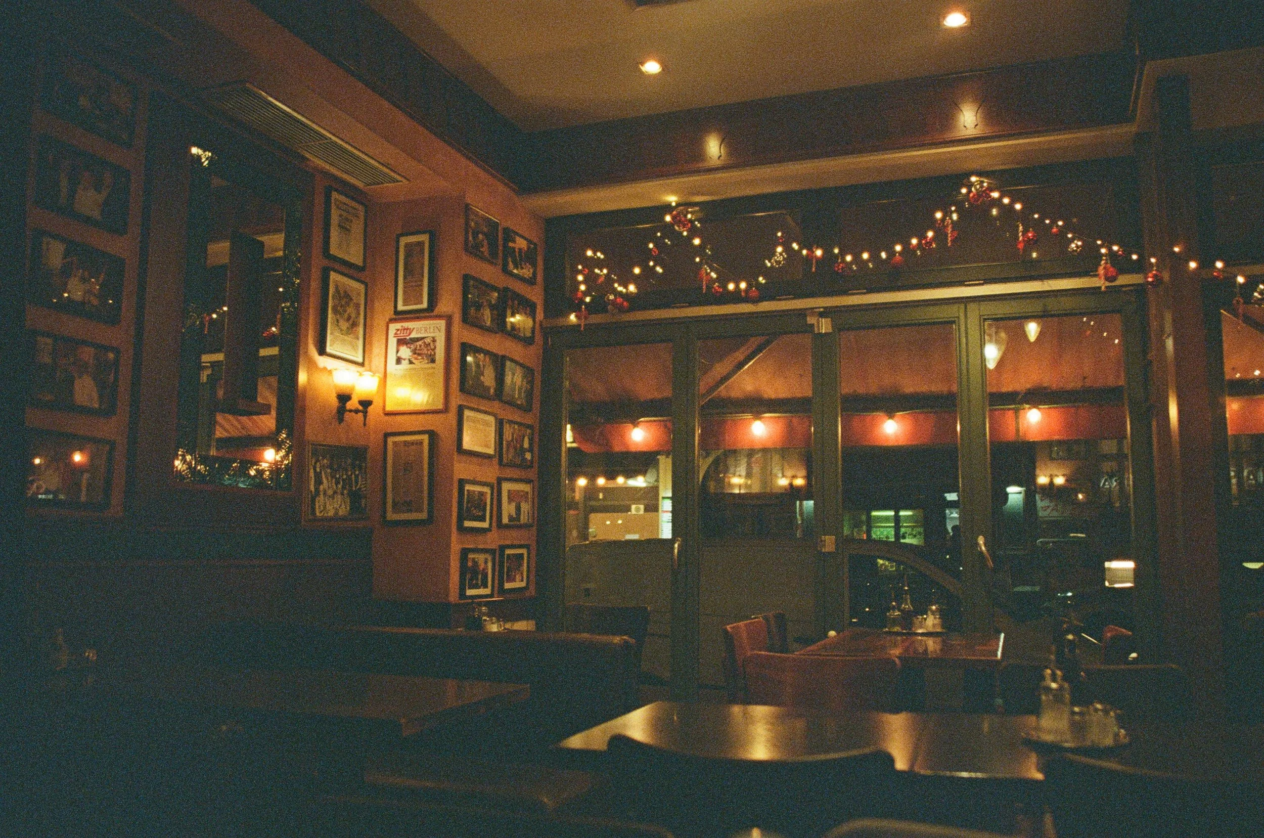 A dimly lit restaurant interior decorated with Christmas garlands and string lights, with framed pictures on the walls and wooden tables and chairs.