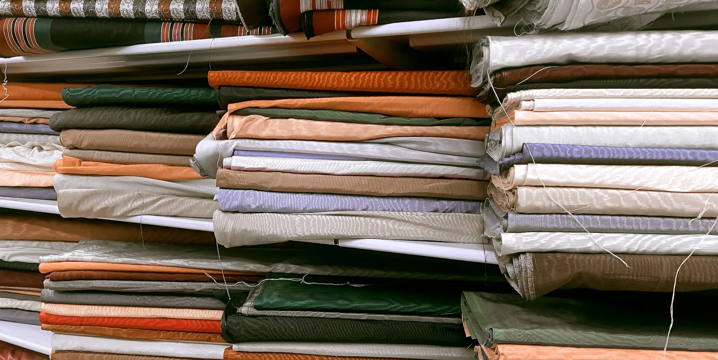 Stacked fabric rolls in various colors and textures on store shelves.