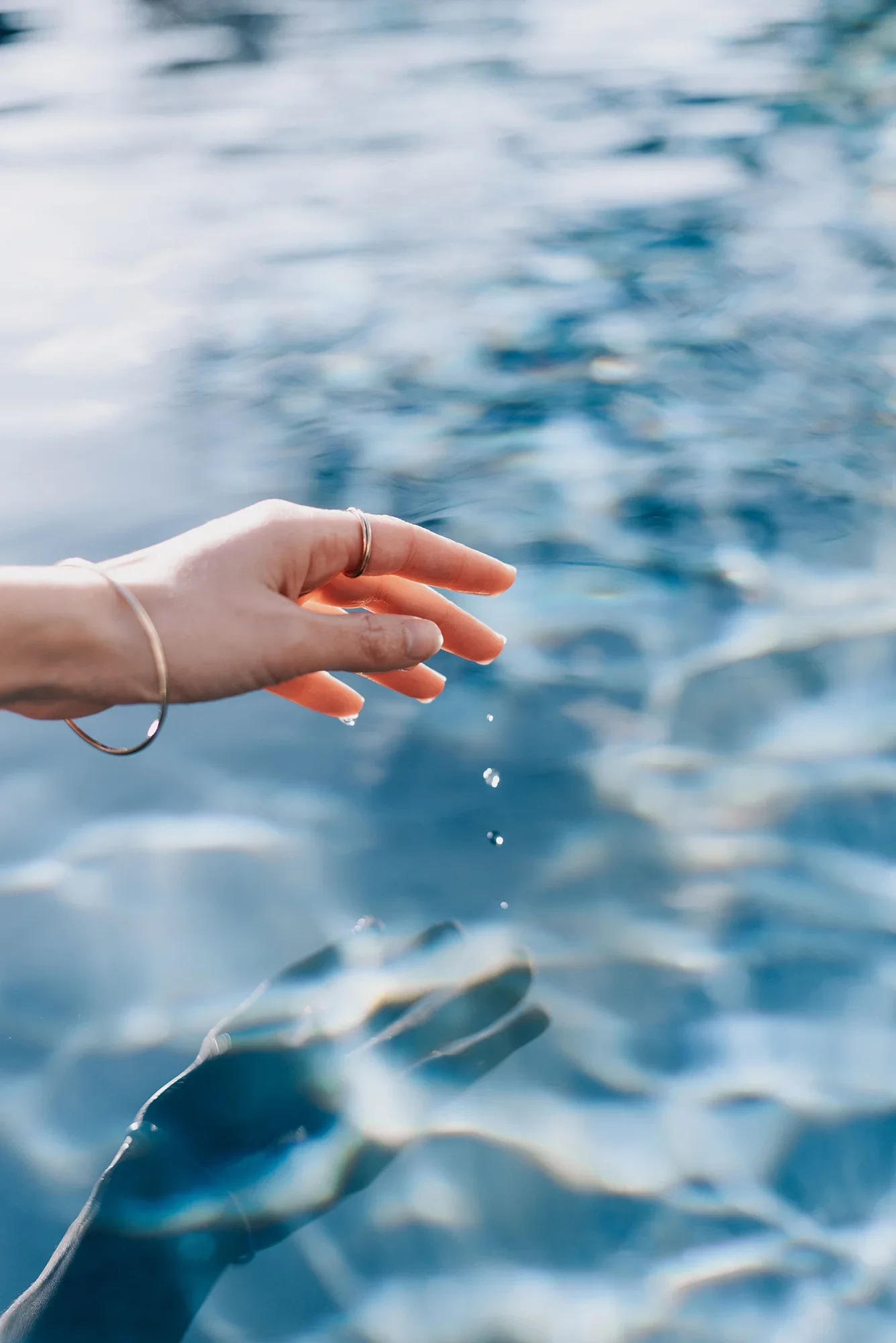woman's hand hovers over pool, water drips from fingers