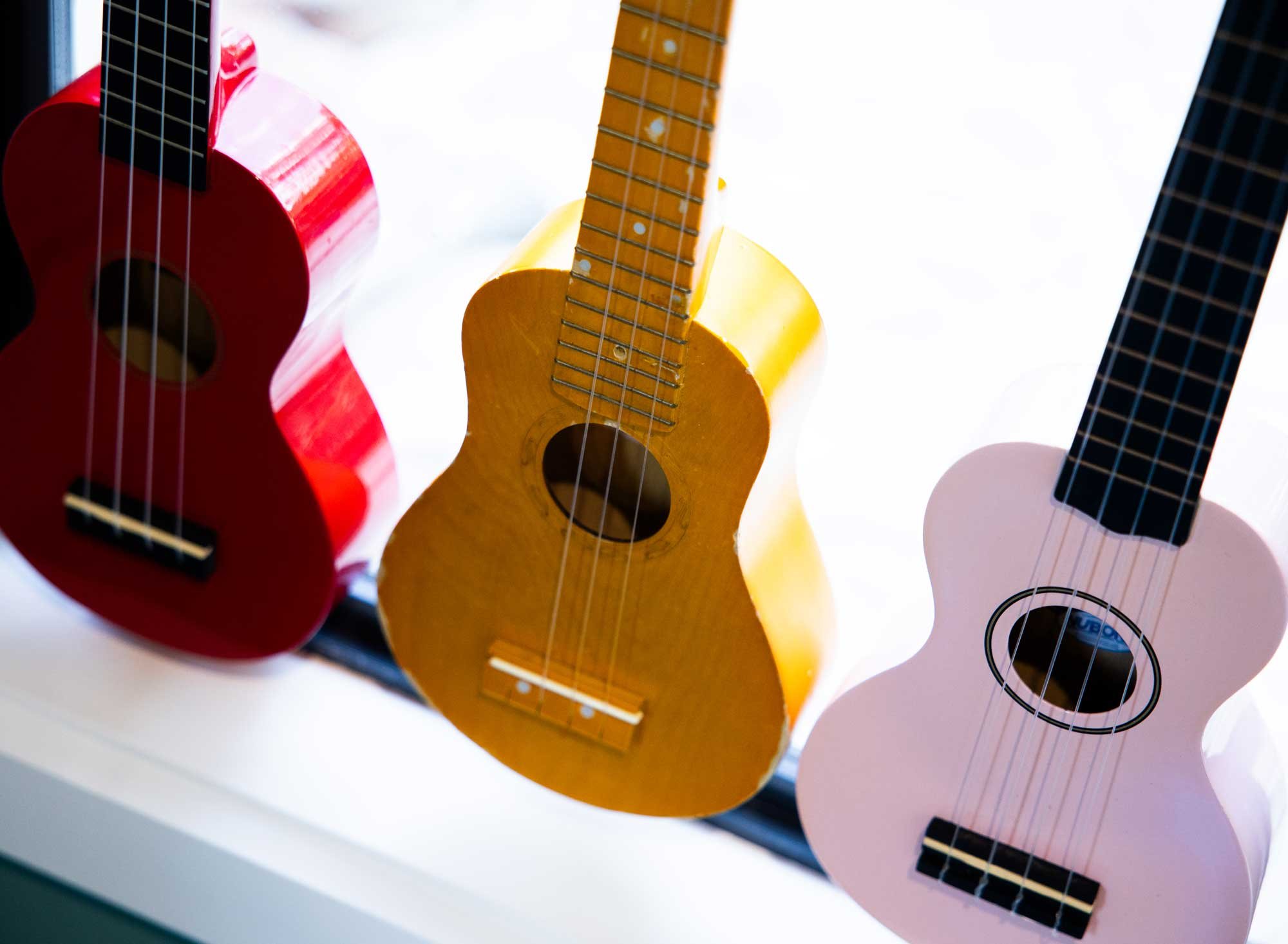 Three colorful acoustic guitars arranged vertically against a white background, with visible strings and sound holes.