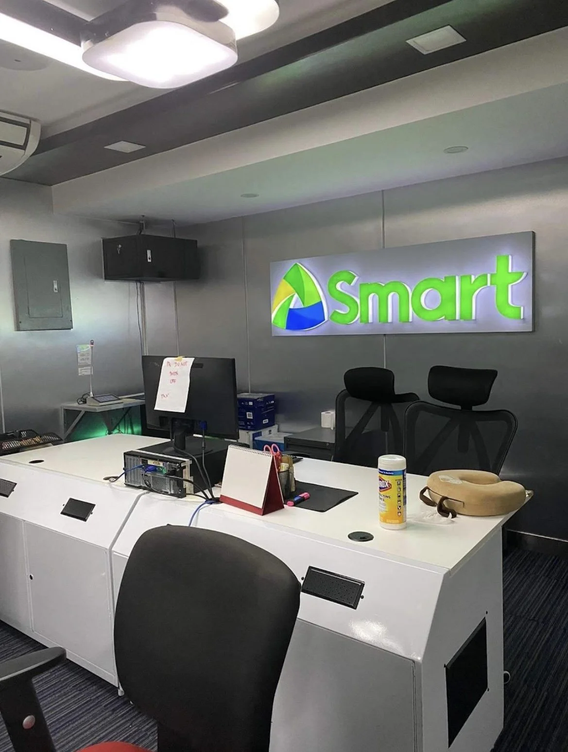 Office reception area with a large illuminated Smart sign on the wall, a desk with computer monitors, office supplies, and a hand sanitizer bottle.