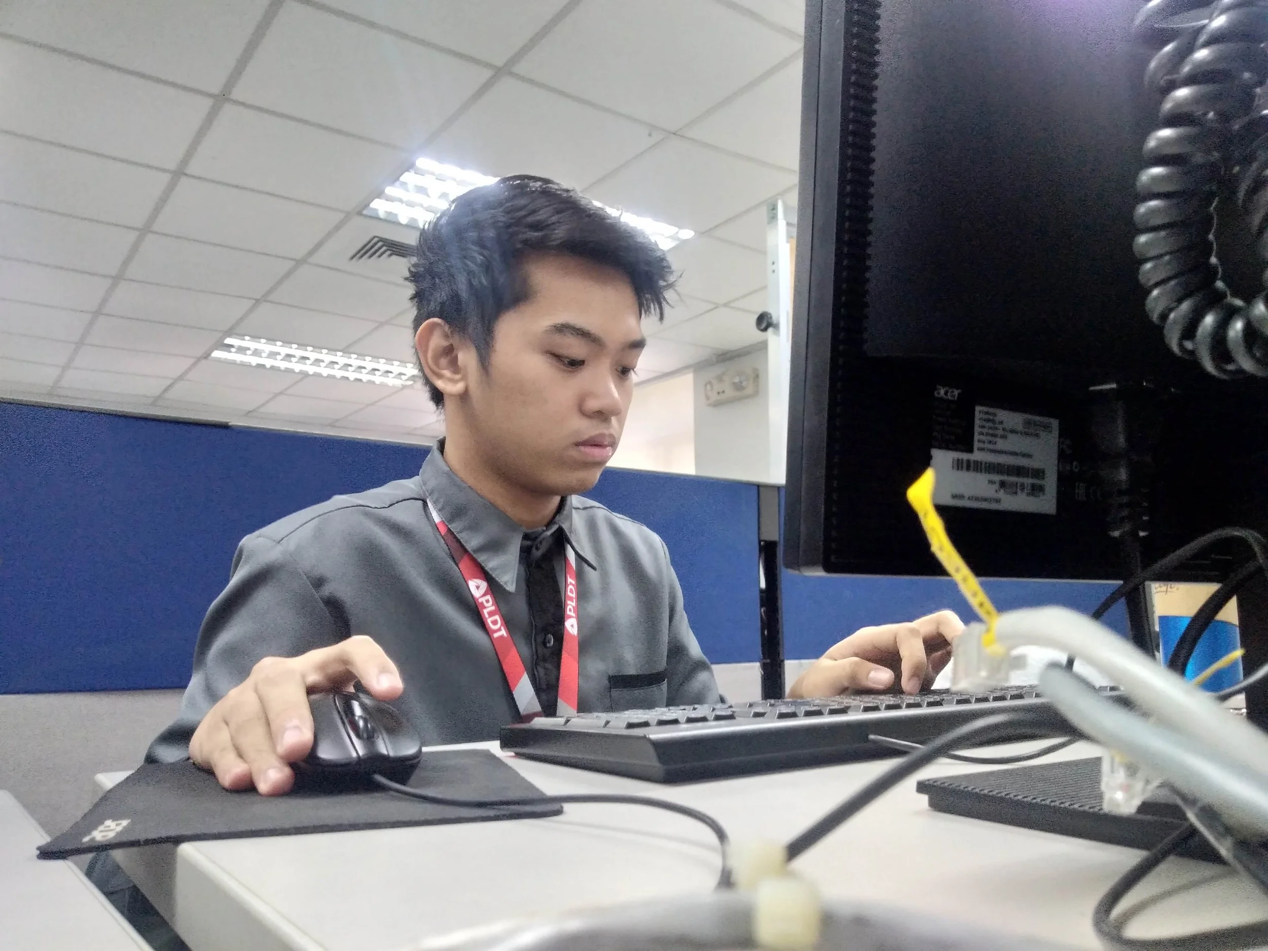 A young man working at a computer workstation in an office environment.