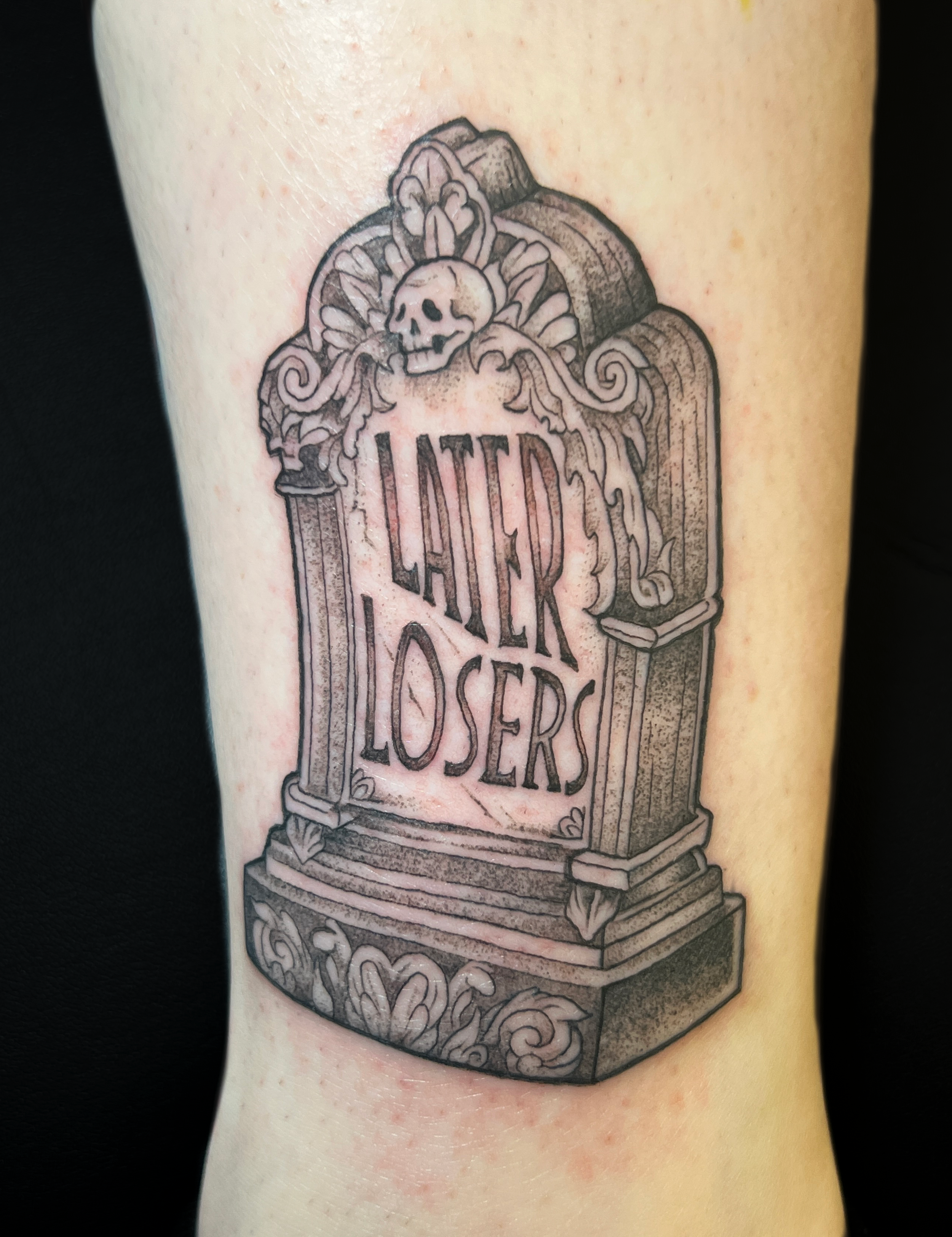 Tattoo of a mausoleum with a skull at the top and ornate carvings, with the words 'LUCASLOSER'.