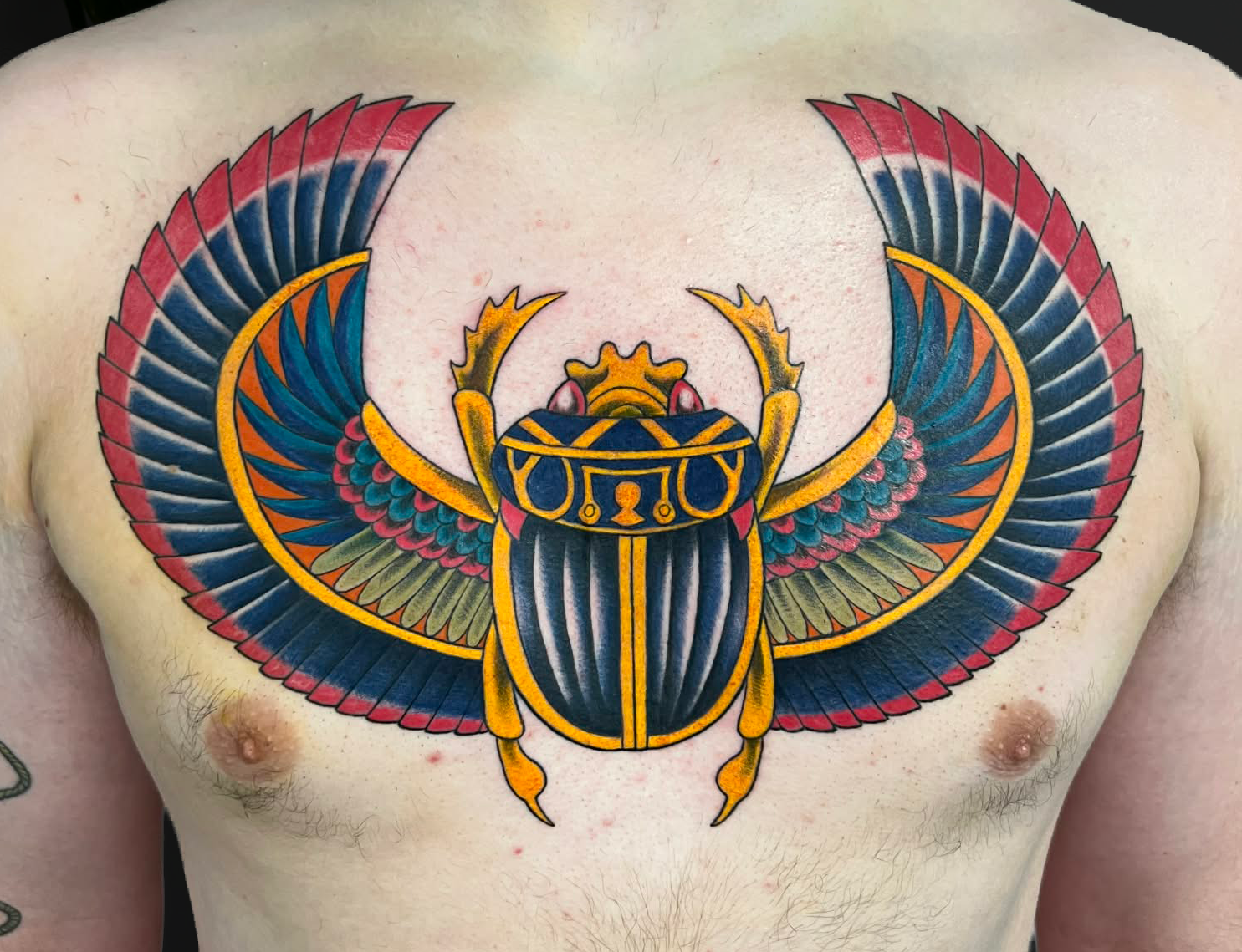 A colorful tattoo of a scarab beetle with outstretched wings on a person's chest.
