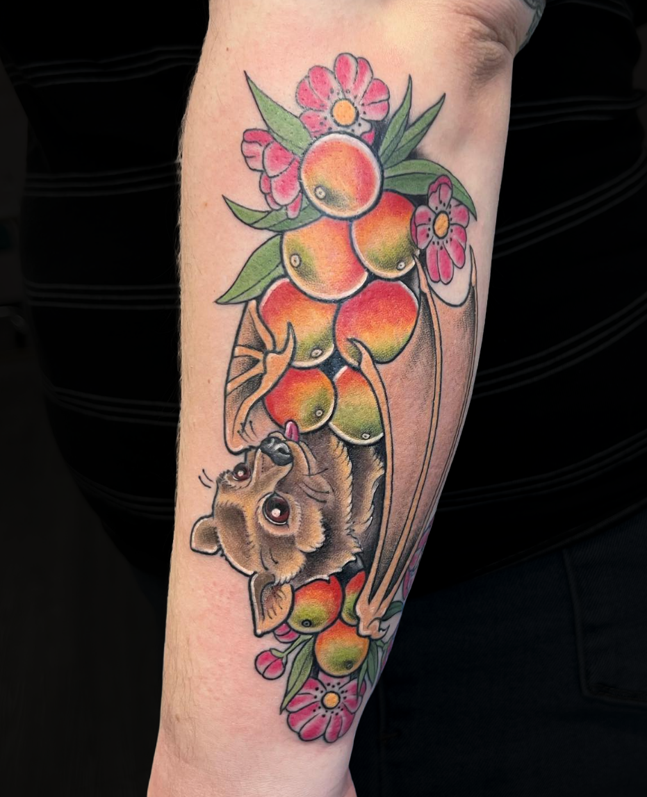Colorful tattoo of a puppy holding a bunch of peaches, surrounded by pink flowers and green leaves on a person's arm.