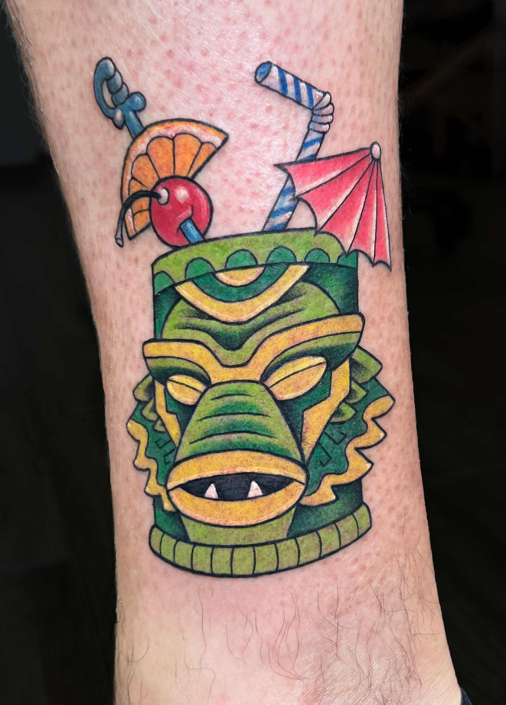 Colorful tattoo of a dragon's head with vibrant green, yellow, red, and orange colors, featuring sharp teeth and menacing eyes, covering a person's forearm.