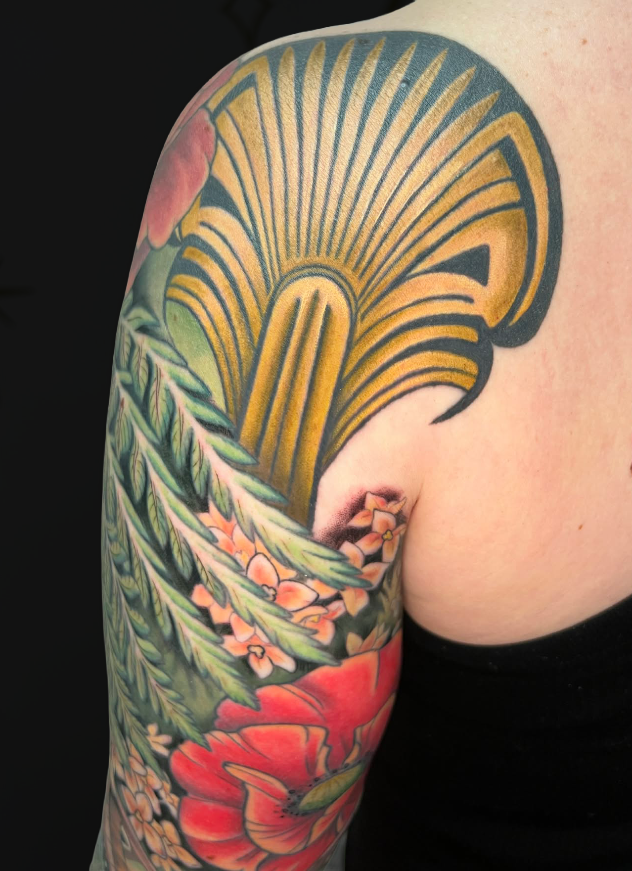 Colorful traditional Japanese style tattoo of a ginkgo leaf, a red poppy flower, and other floral elements on a person's arm.