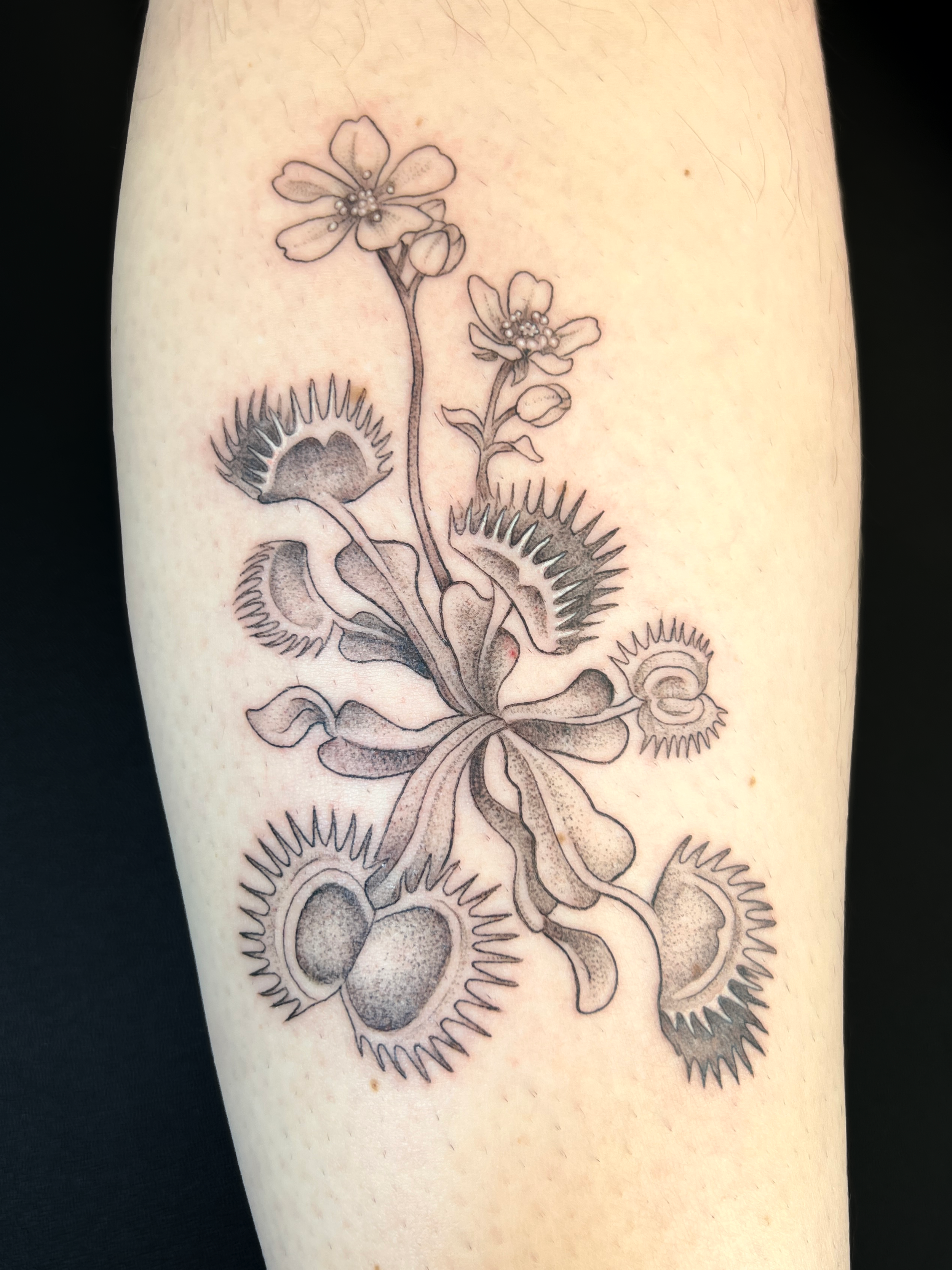Black line drawing of a floral tattoo on skin, featuring flowers, buds, and leaves with detailed shading.