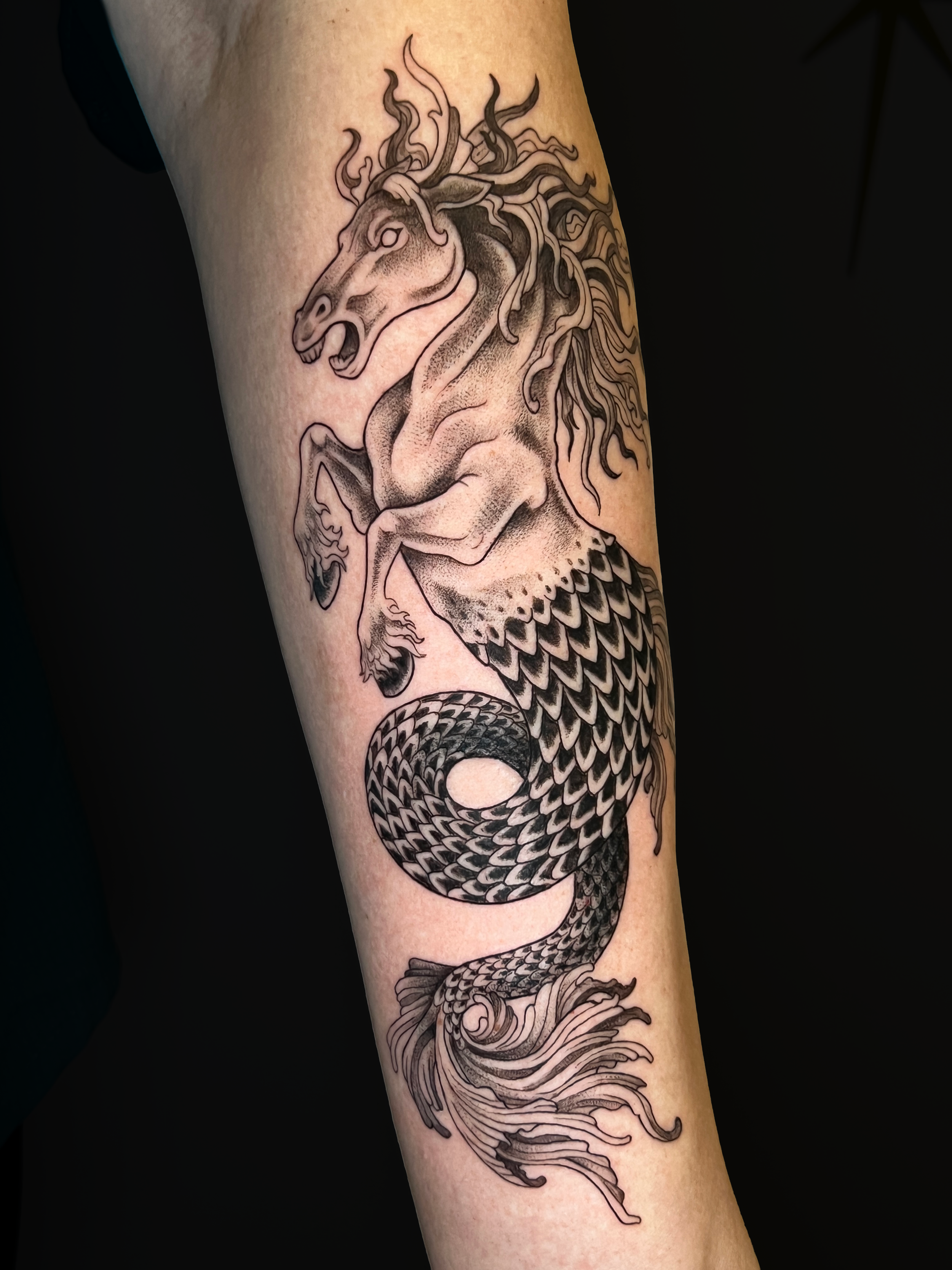 Black and gray tattoo of a roaring dragon with intricate scales and flowing flames on a person's arm.