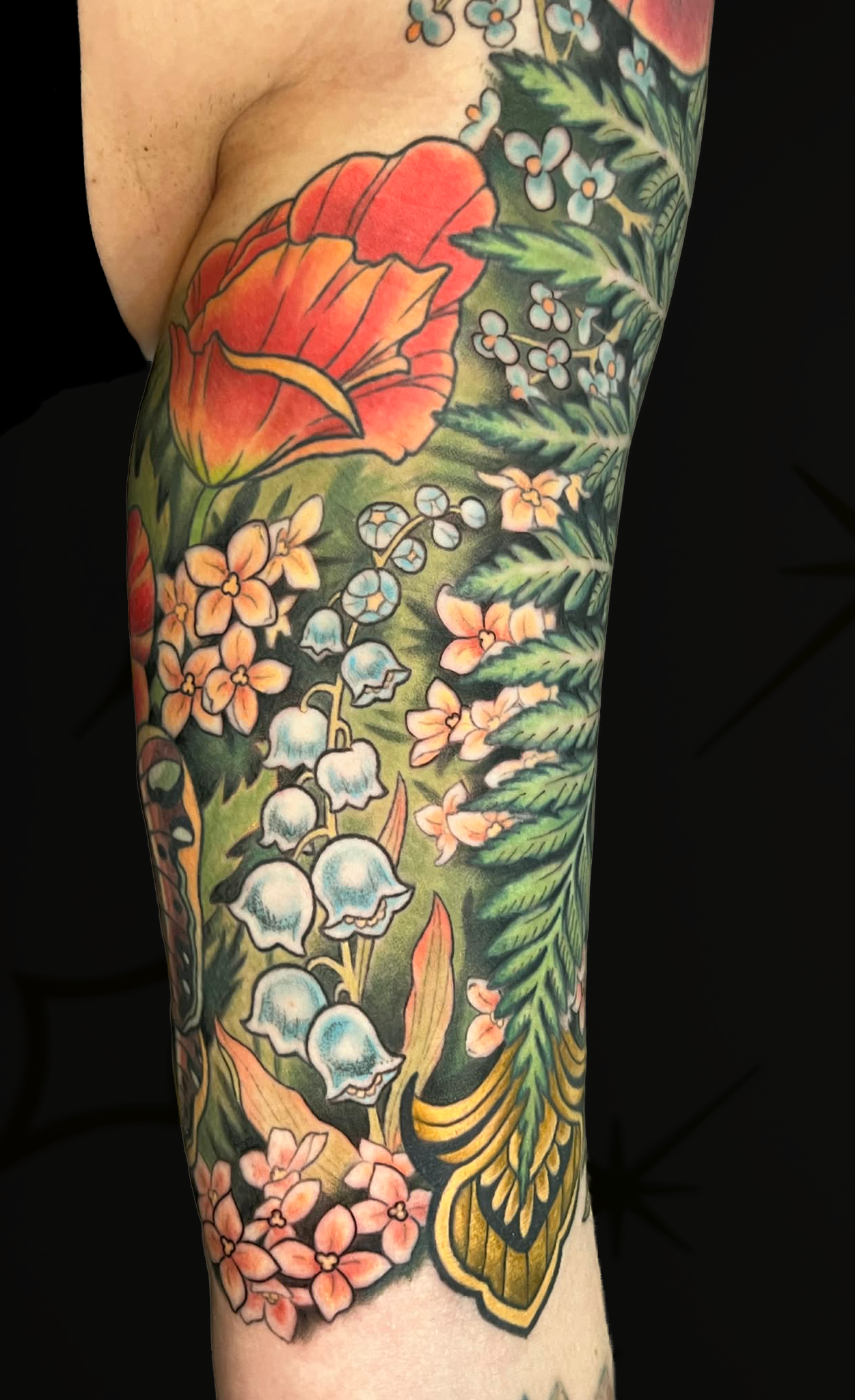 Colorful floral tattoo featuring orange and pink flowers, white bell-shaped flowers, green leaves, and yellow accents on skin.