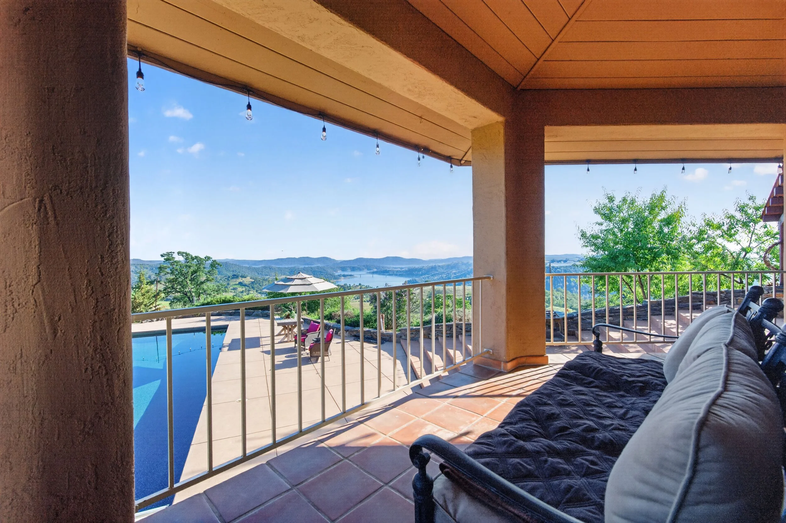 Elevated outdoor entertaining space at Airola Ranch featuring panoramic foothill scenery, poolside lounge areas, and lake views.