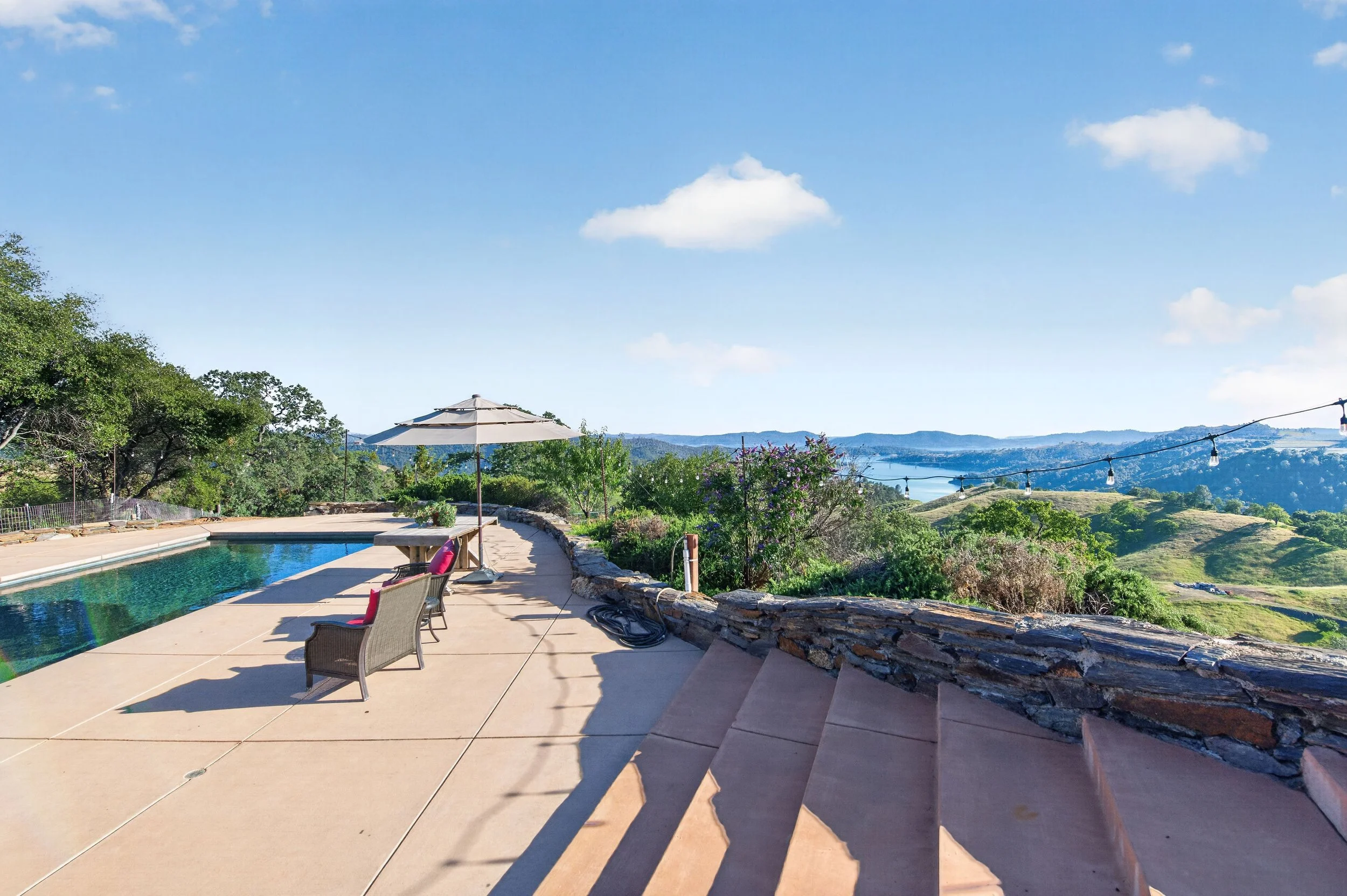 Luxury outdoor gathering space and pool near Murphys and Angels Camp with poolside seating, string lighting, and scenic countryside and lake views.