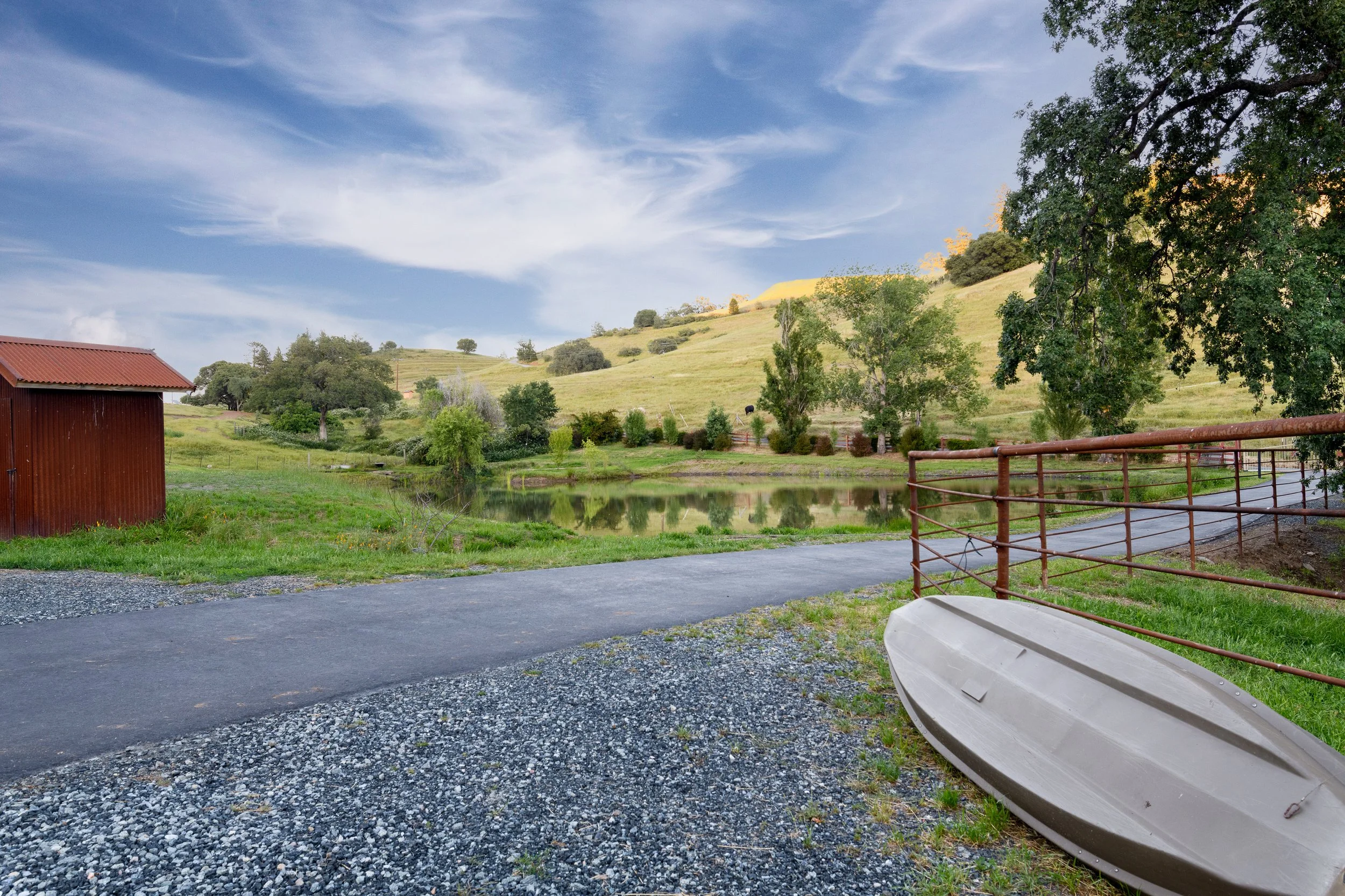 A peaceful rural scene with a small pond, grassy hills, trees, a red barn, and a cloudy sky.