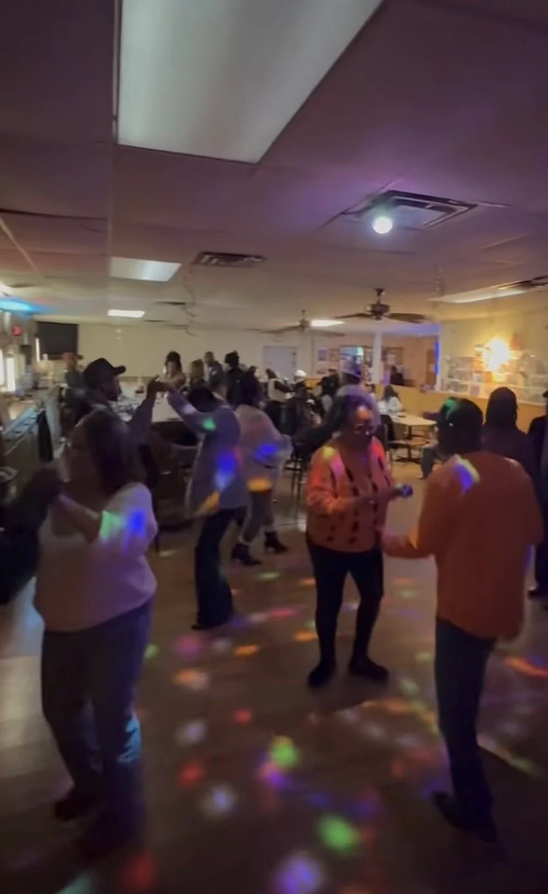 People dancing and socializing in a dimly lit room with colorful disco lights on the floor and ceiling.