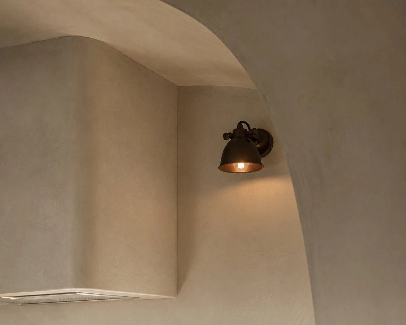 A black wall-mounted light fixture illuminating a textured beige wall in an interior space.