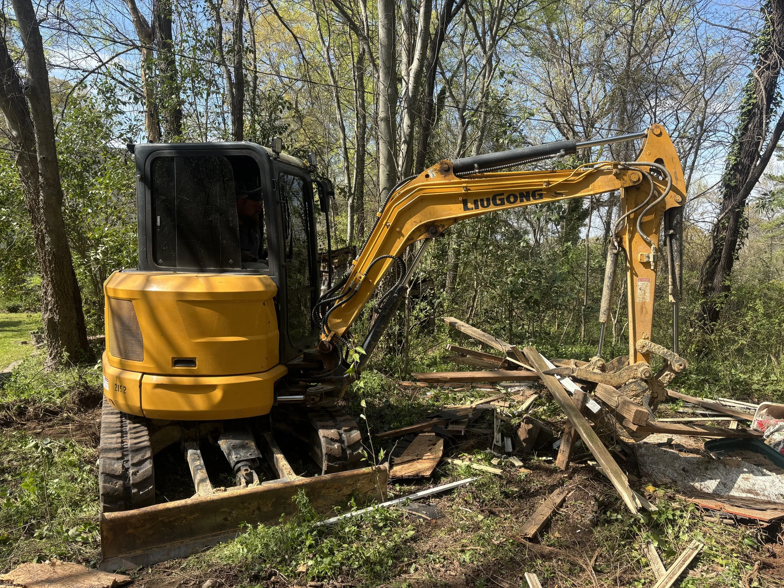 A yellow and black excavation bulldozer working on a wooded land clearing project, with trees and debris around.