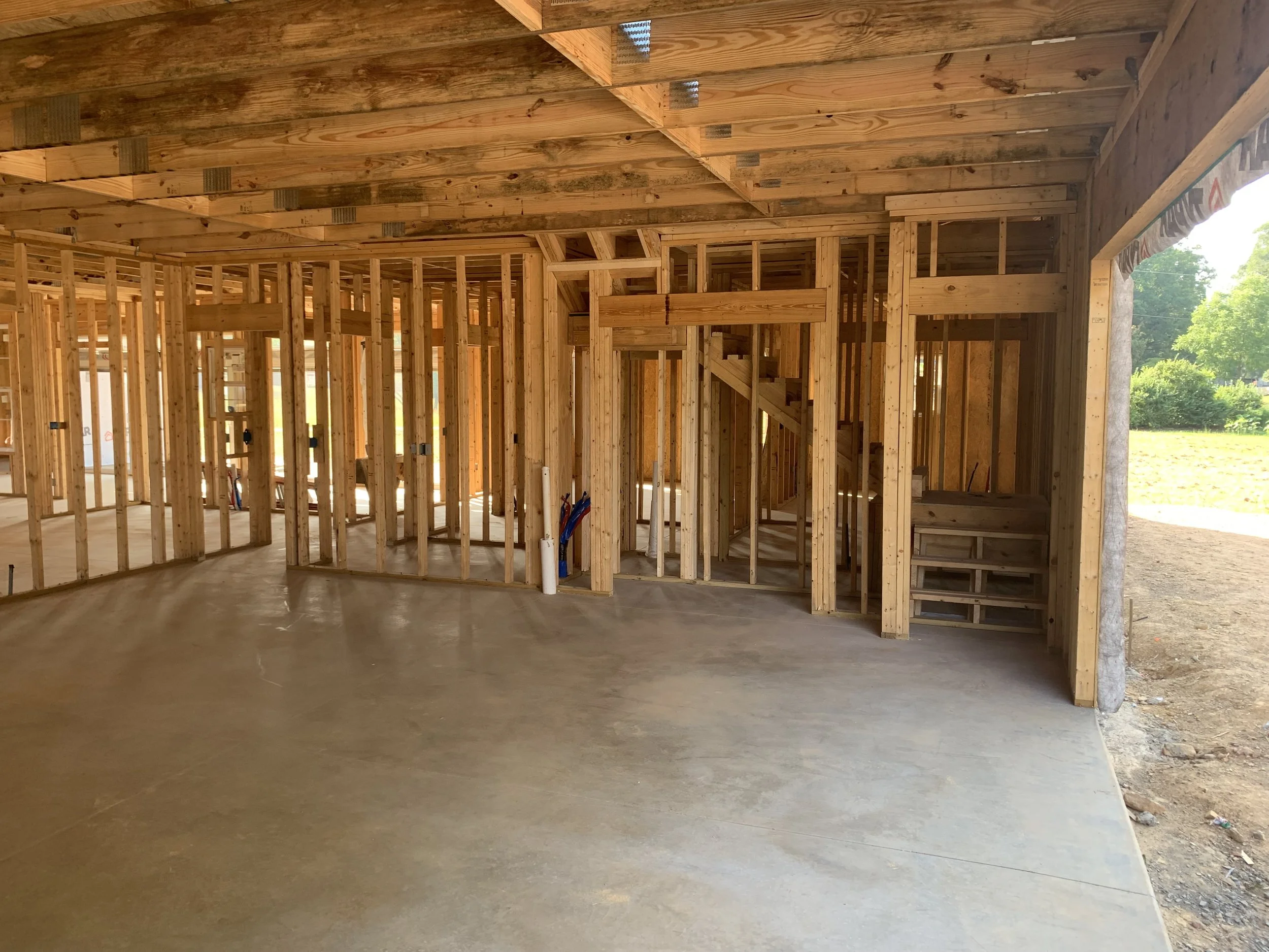 Interior view of a house under construction showing wooden framing and a concrete floor with no drywall installed yet.