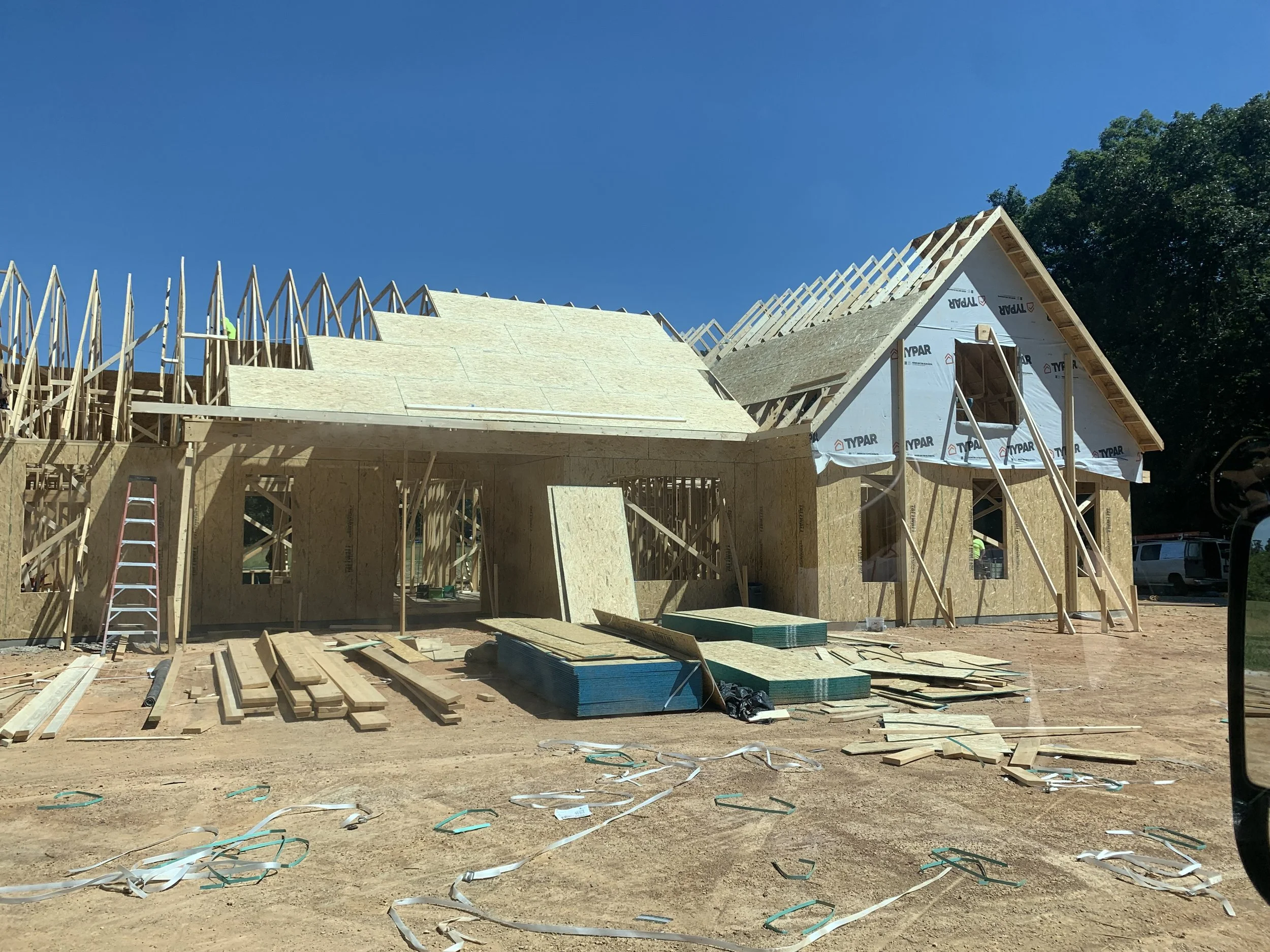 Under construction house with wooden framing, plywood walls, and roofing in progress under a clear blue sky.