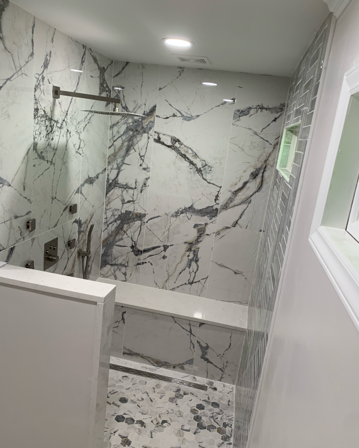 Modern bathroom shower area with marble wall tiles, a small window, and pebble mosaic floor tiles.