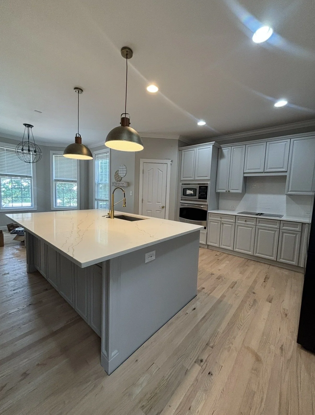 A modern kitchen with white cabinetry, a large marble island with a gold faucet, wood flooring, and multiple ceiling lights.
