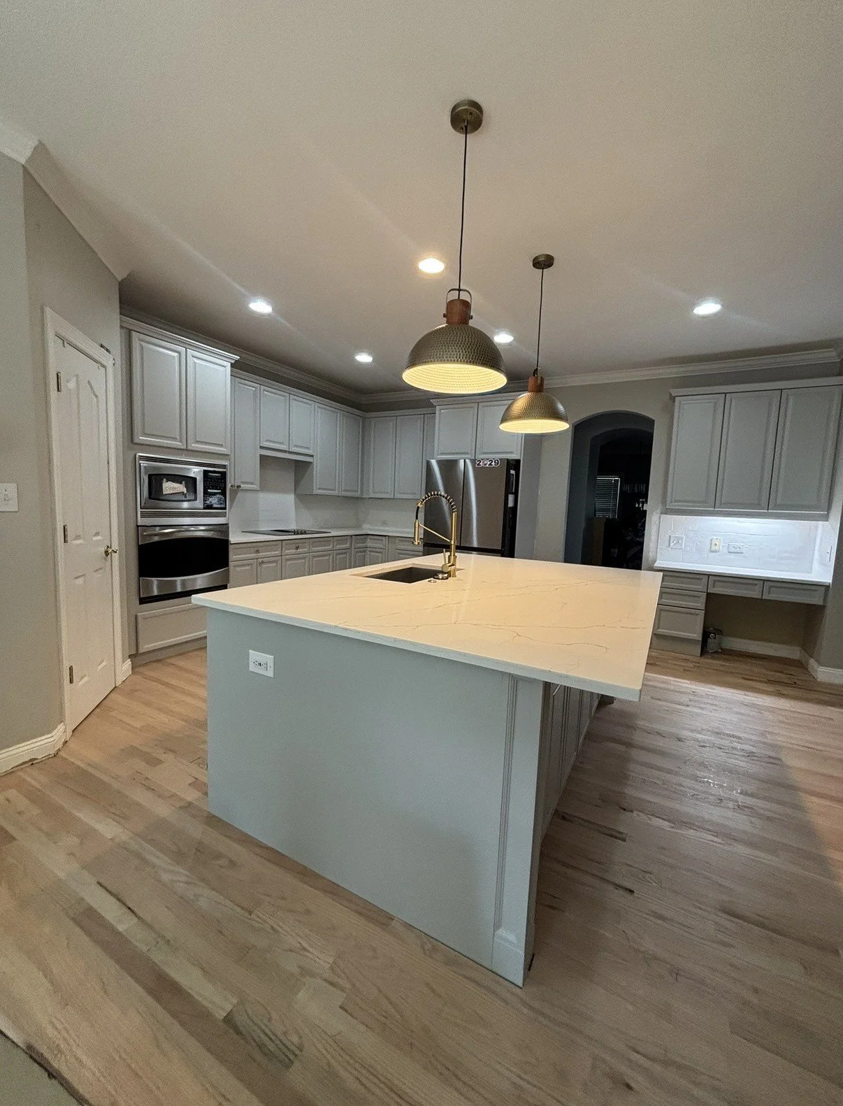 Modern kitchen with white cabinets, a large island with a white marbled countertop, stainless steel appliances, and pendant lights hanging over the island, with hardwood flooring.