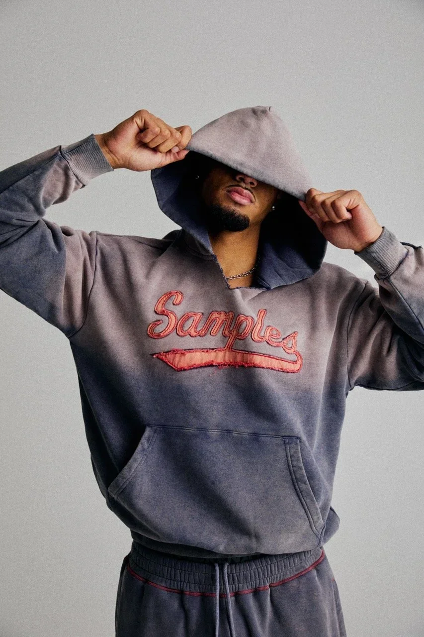 Man wearing a hoodie with the word 'Samples' on it, pulling the hood over his face.