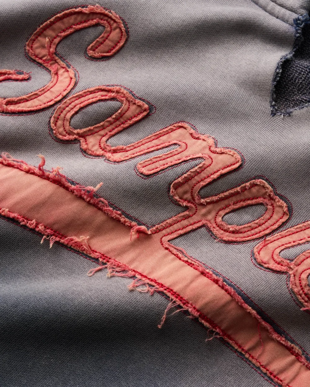 Close-up of gray fabric with frayed edge and embroidered pink and coral text.