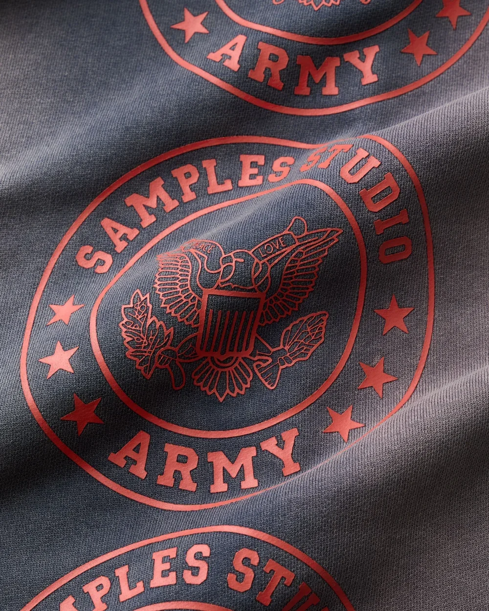 Close-up of a gray fabric with red printed US Army emblem, featuring an eagle holding a shield with the word "LOVE" and surrounded by stars and the words "SAMPLE STUD ID" and "ARMY."
