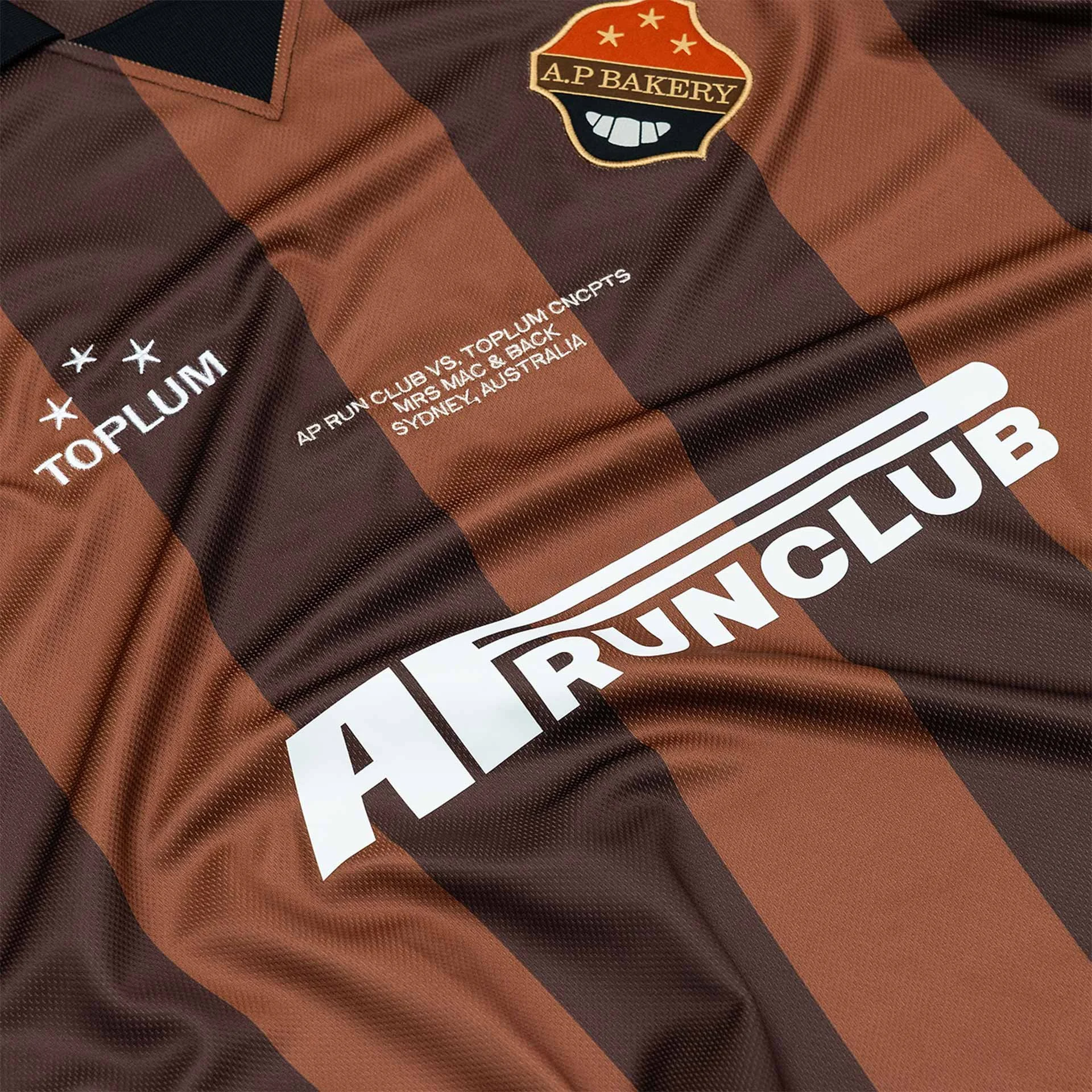 Close-up of a brown and black checkered sports jersey with an embroidered badge reading "A.P. Bakery" and a partially visible white sponsor logo.
