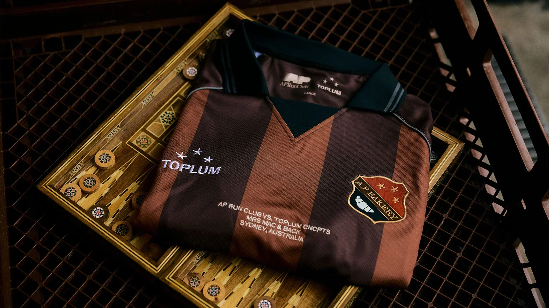 A folded maroon and black striped sports jersey with team logos and sponsors, resting on a rectangular wooden backgammon board with game pieces, inside a shopping cart.